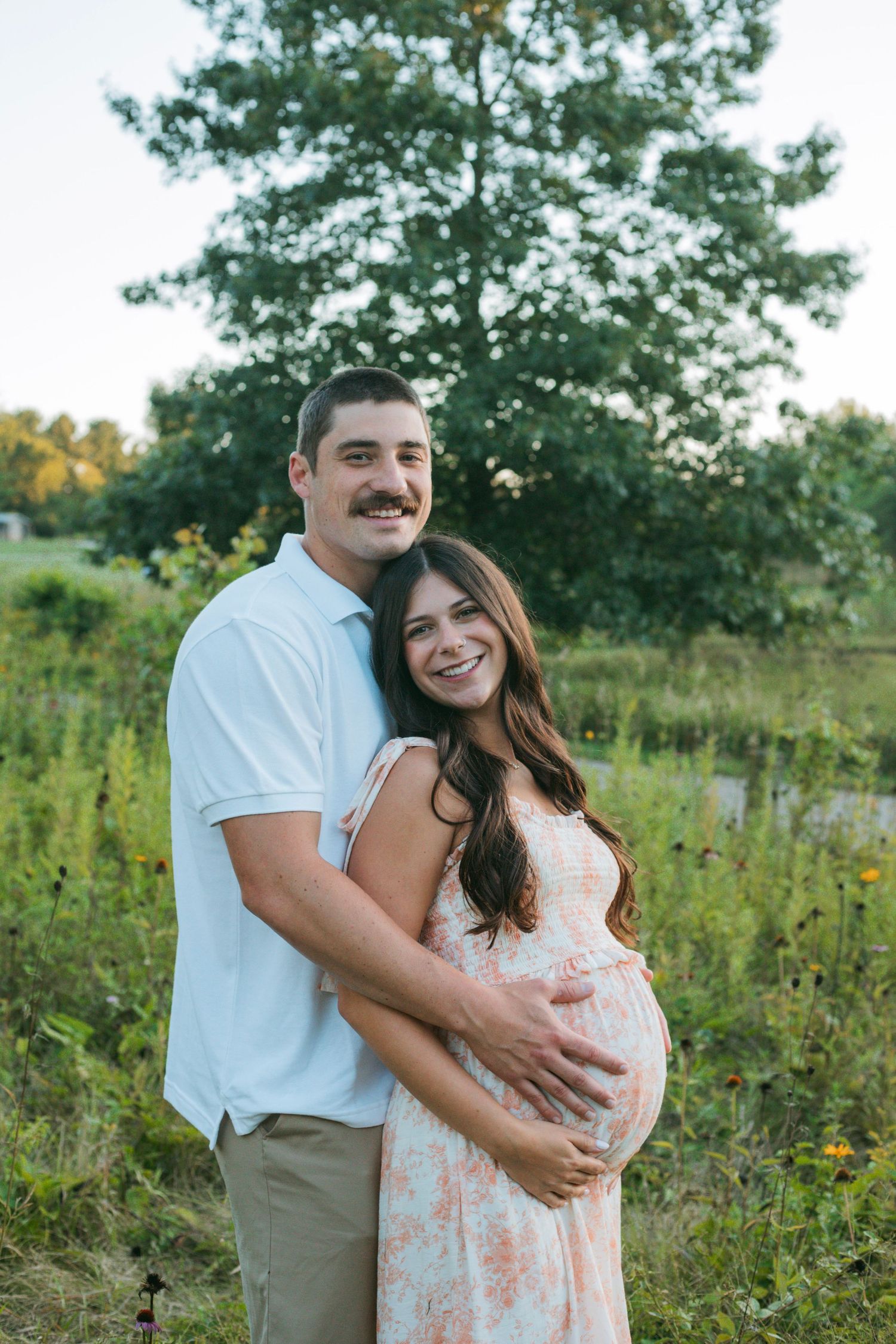 Smiling expectant couple posing together in colorful wildflower meadow during golden hour maternity session.