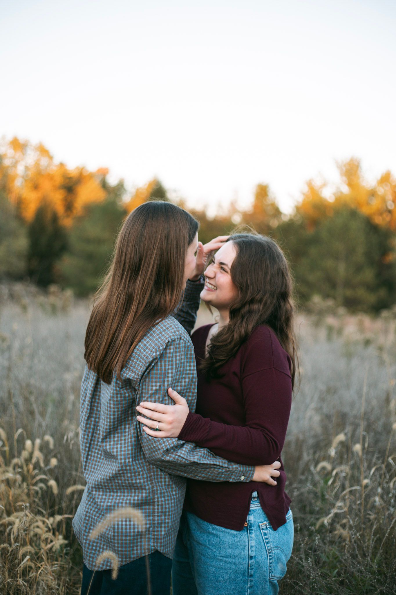 Two women with brown hair embracing and kissing in an autumn field at golden hour.