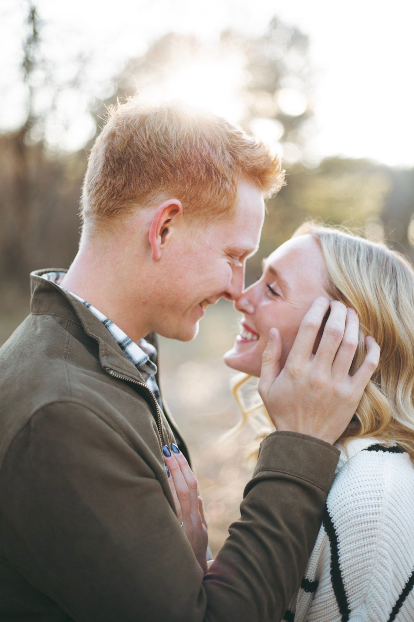 Smiling couple sharing a romantic nose-to-nose moment outdoors in warm golden sunlight.