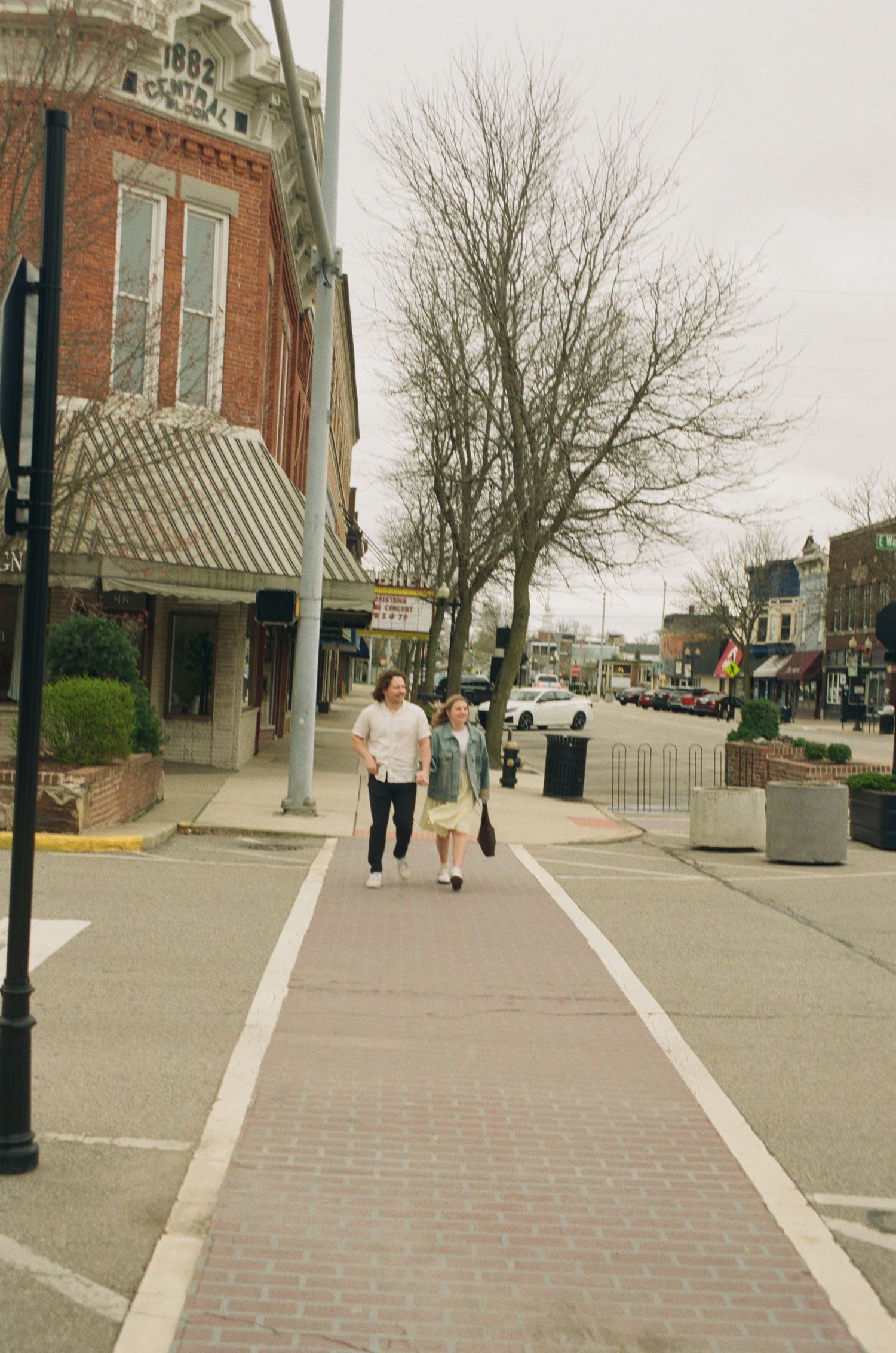 Two people walking on a brick sidewalk in a small town on a cloudy day.