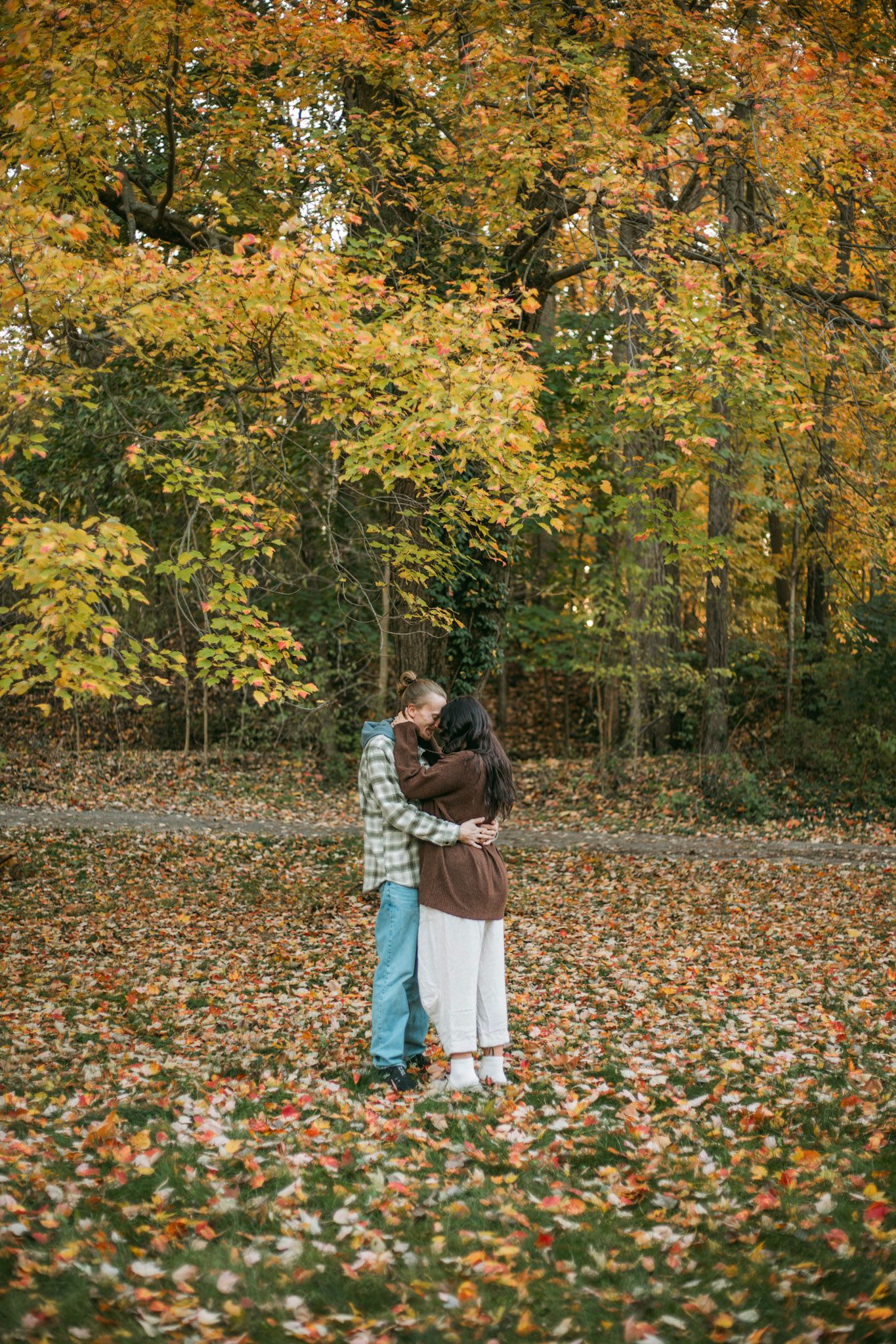 Couple hugging surrounded by vibrant fall foliage in an autumn park setting.