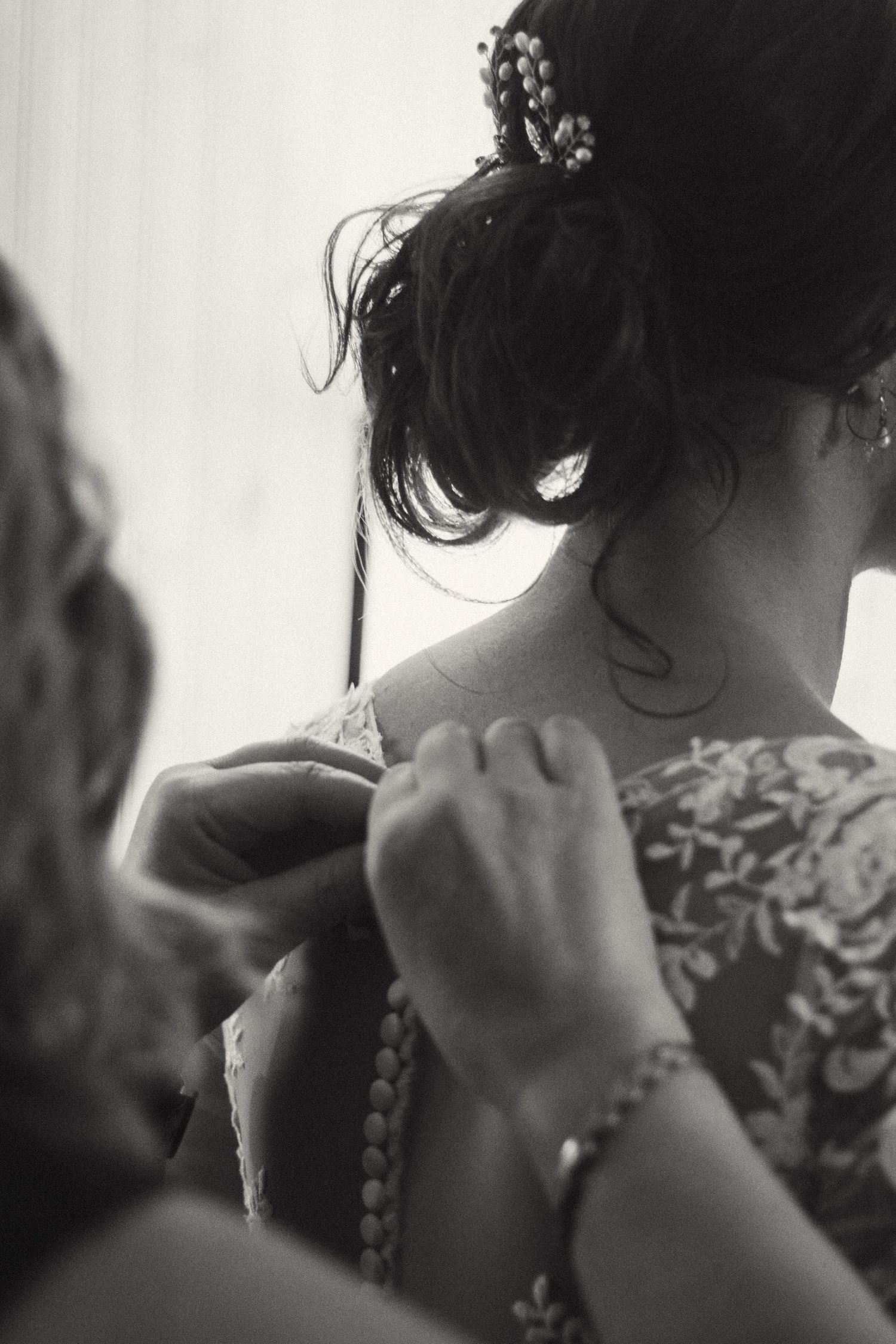 Black and white photo of a woman having her dress fastened with flowers in her updo hair.