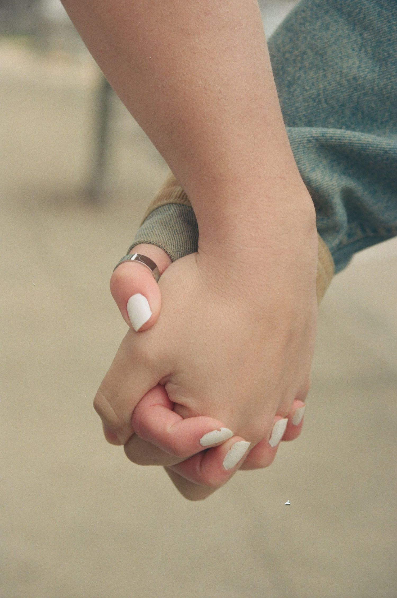 Close-up of a couple holding hands, woman wearing white nail polish and a silver ring.