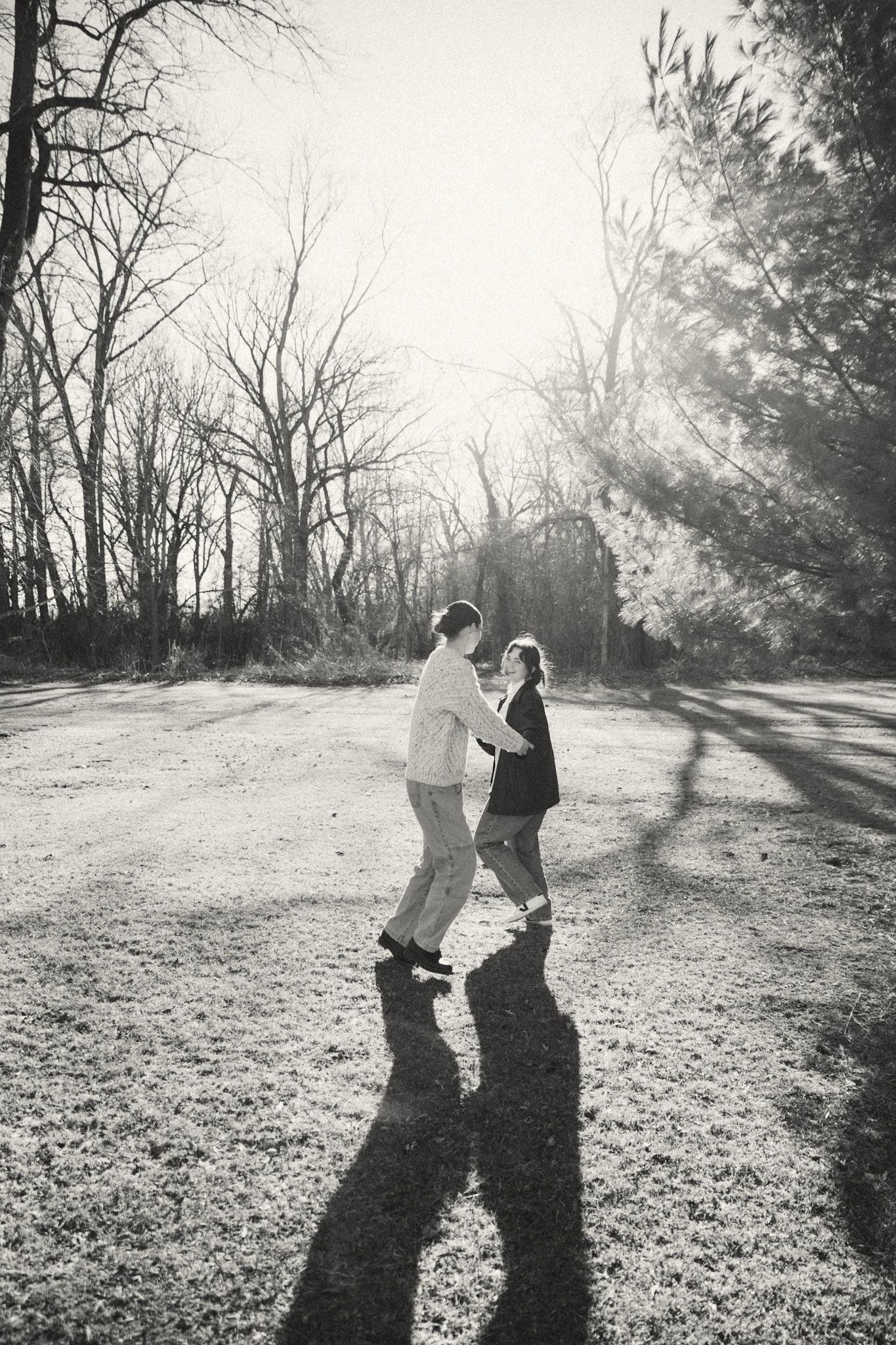 A black and white photo of a couple dancing together in an open sunlit outdoor space.