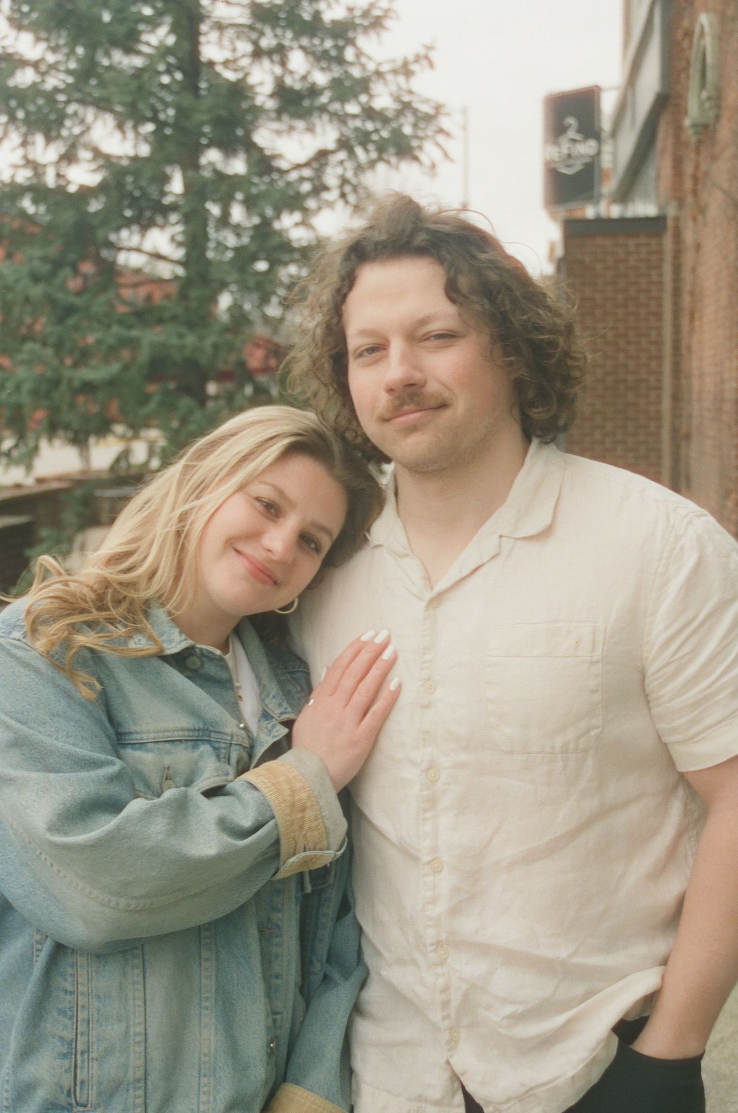 Close-up portrait of happy couple, woman in denim jacket resting head on mans chest outdoors.