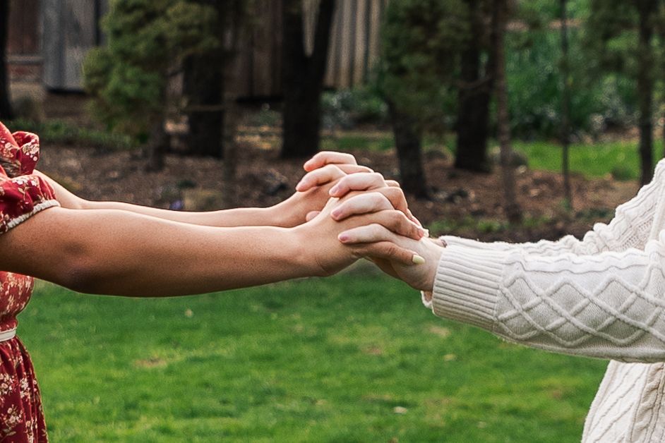 Close-up of couple holding hands together outdoors with green grass in the background.