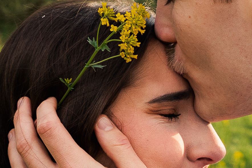 Romantic close-up of man kissing woman's forehead with yellow wildflowers in her dark hair.