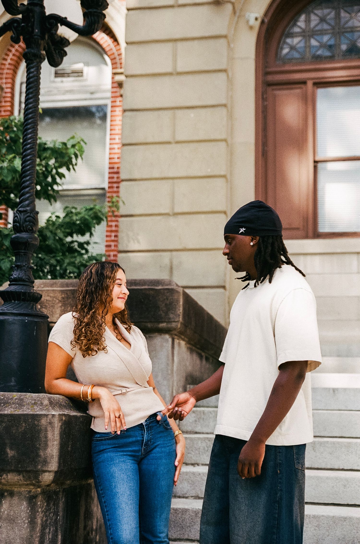 Two young people having a conversation outdoors near historic stone building steps and ornate lamppost.