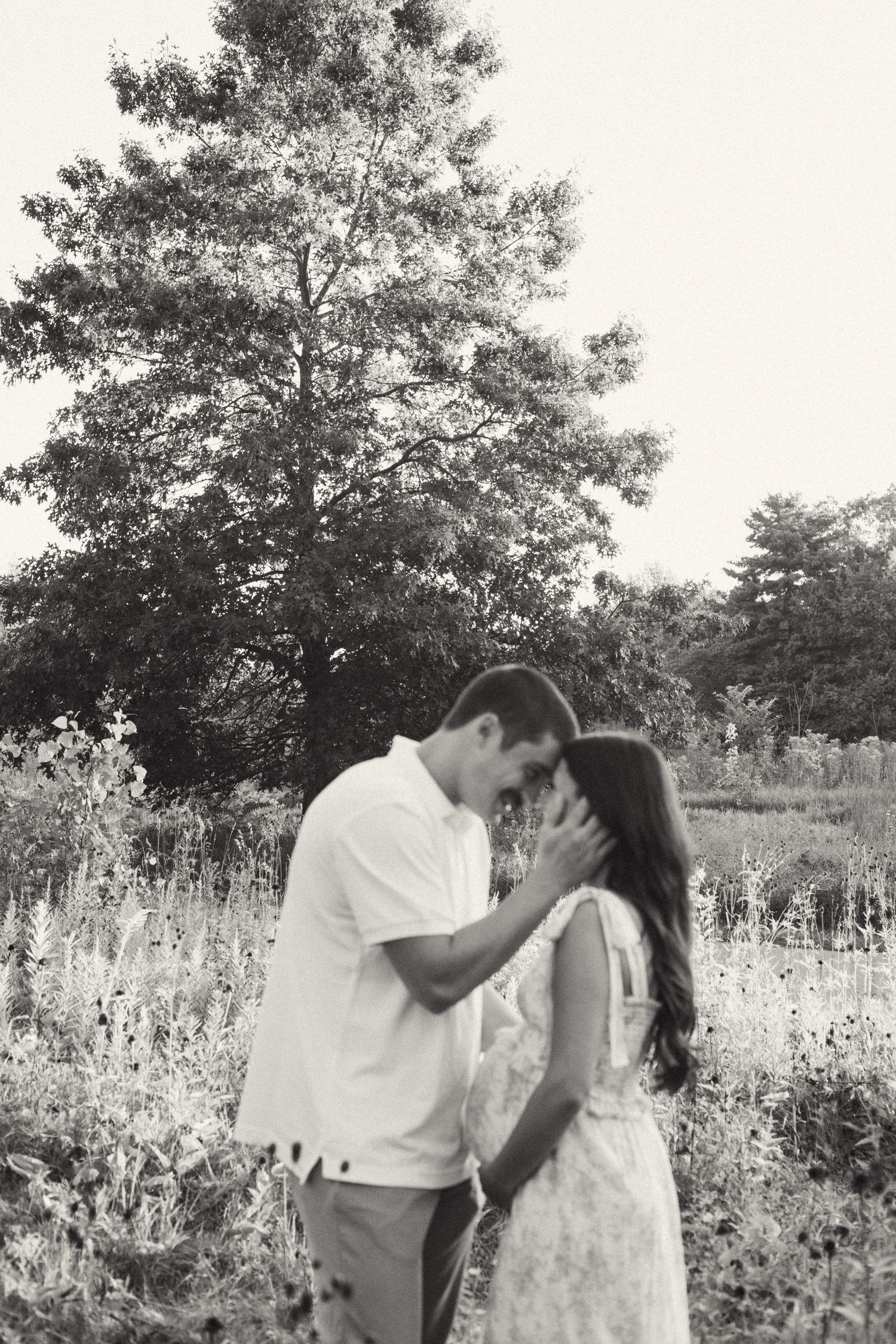 Black and white romantic maternity photo of couple sharing intimate moment in lush wildflower field.