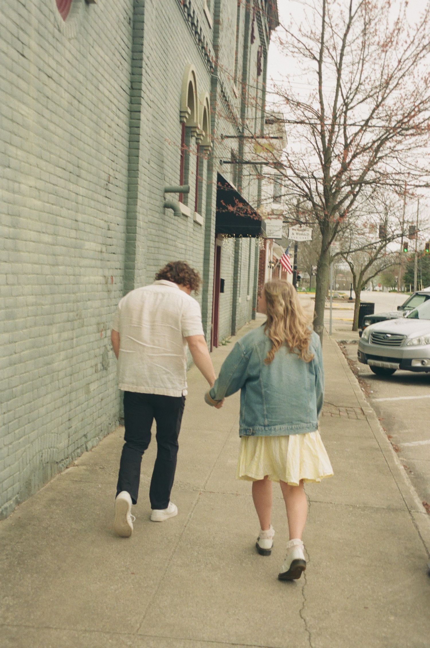 Couple walking hand in hand along a brick sidewalk past historic buildings with an American flag.
