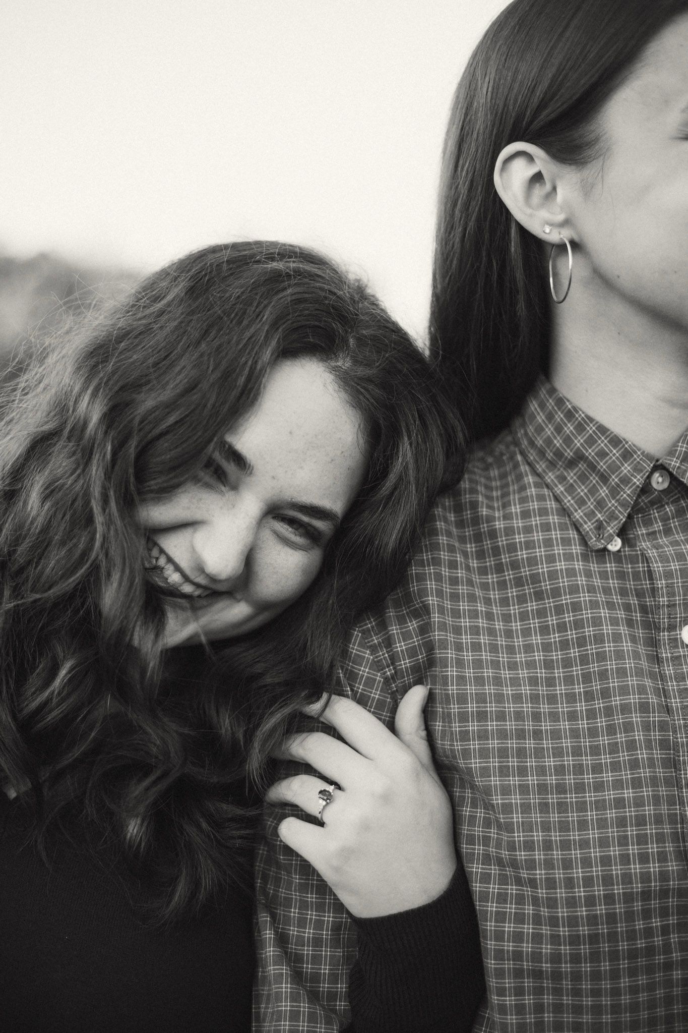 Black and white photo of a laughing woman leaning on a man's shoulder outdoors.
