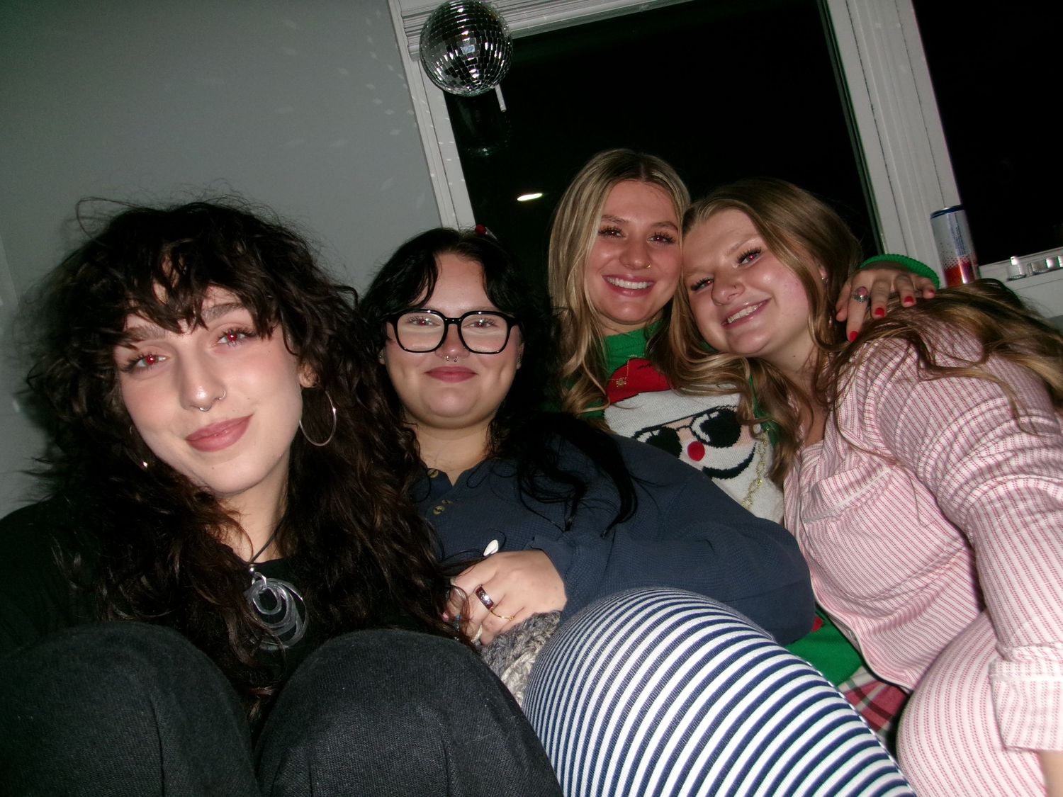 Four smiling women posing together at a festive holiday gathering, one wearing an elf headband.