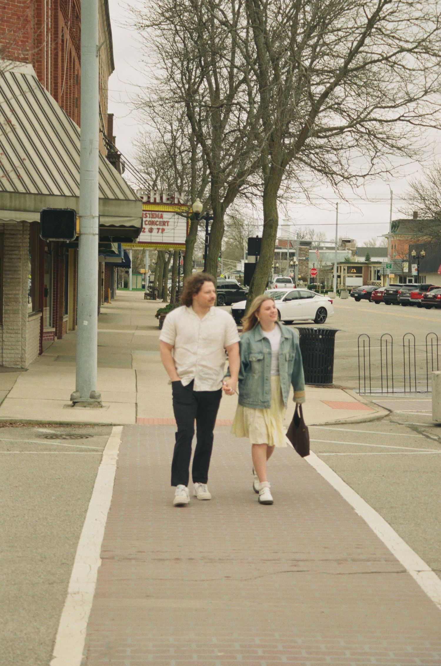 Couple walking together on a downtown sidewalk near a theater marquee on a cloudy day.