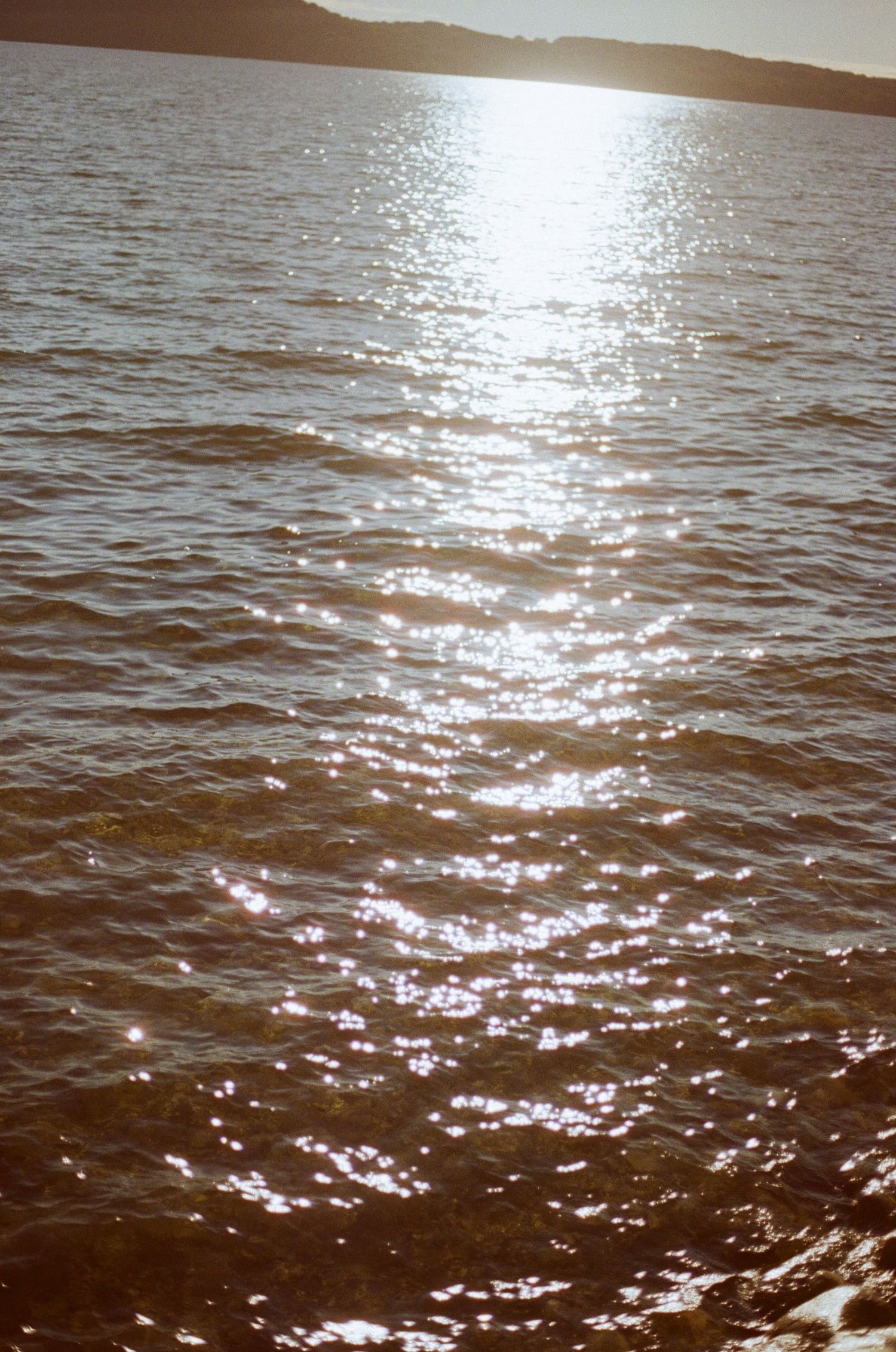 Sunlight sparkling on rippling lake water with silhouetted hills in the background at golden hour.