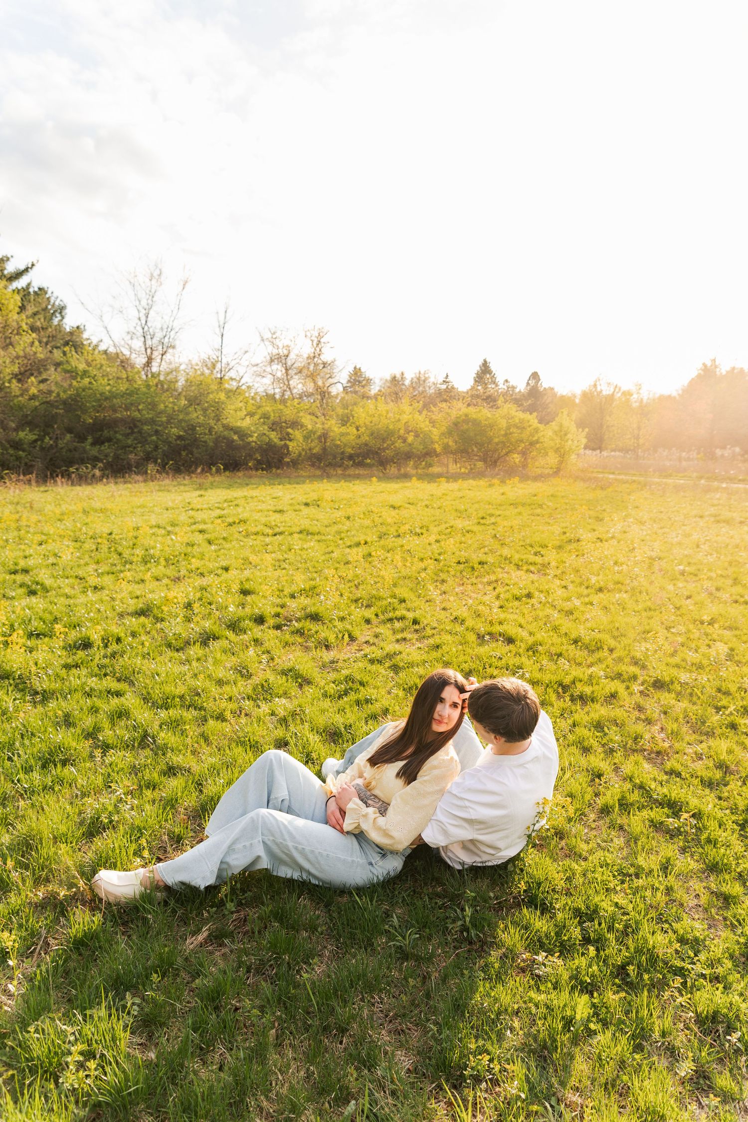 Couple sitting together in a sunlit green meadow, woman leaning against man outdoors.