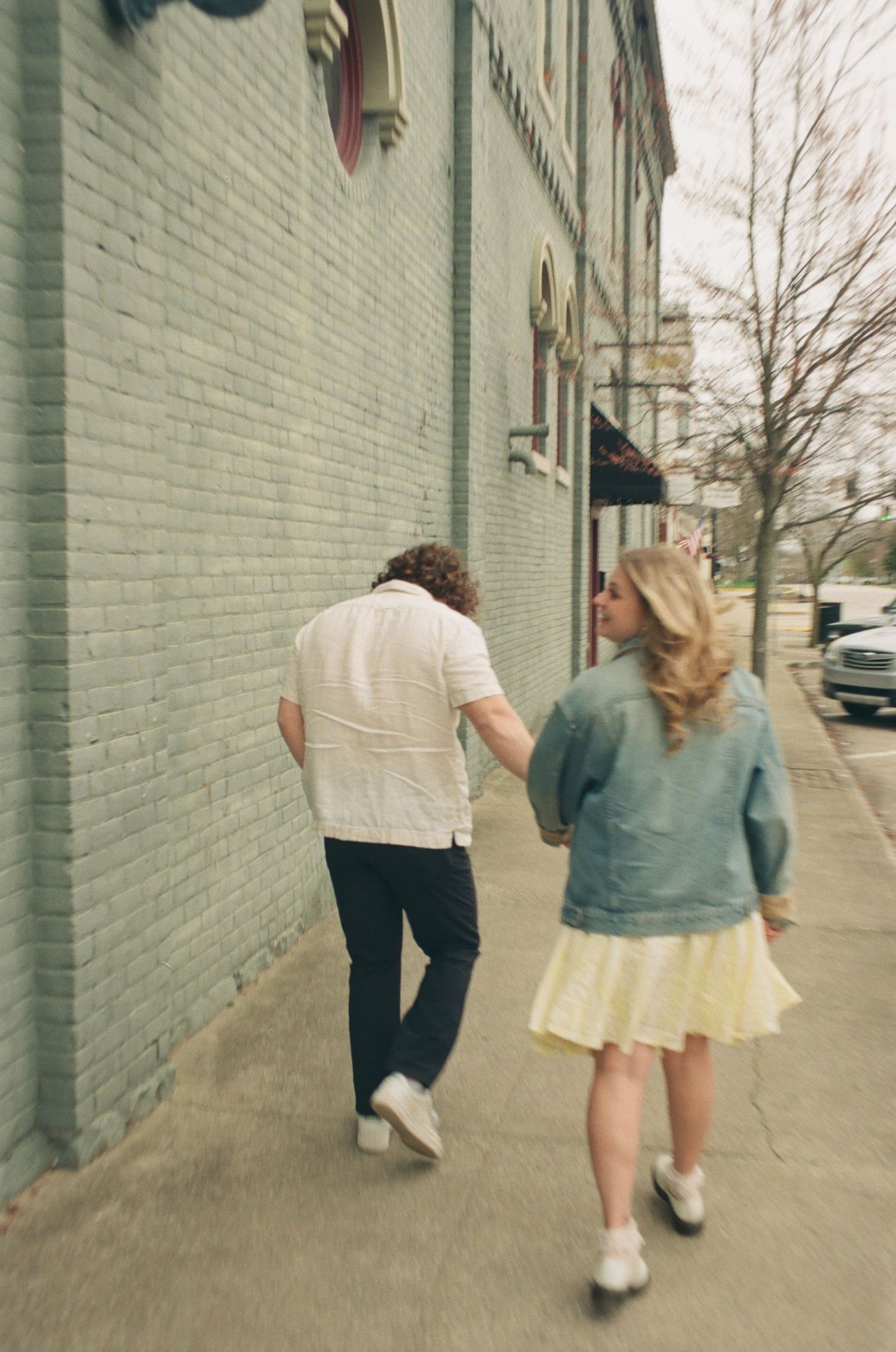 Couple holding hands while walking along a historic brick building sidewalk in a small town.