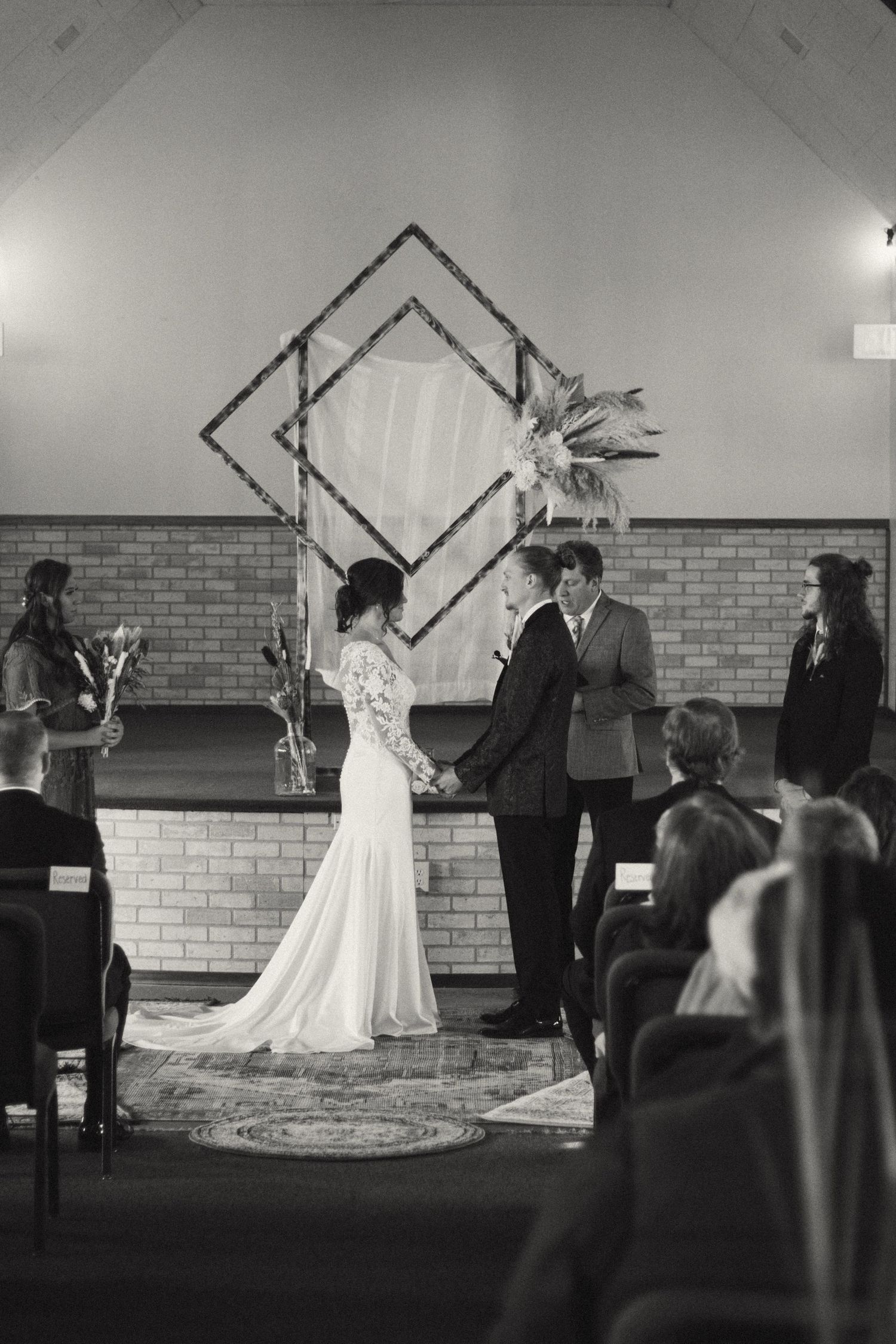 Black and white photo of bride and groom exchanging vows at an indoor wedding ceremony altar.