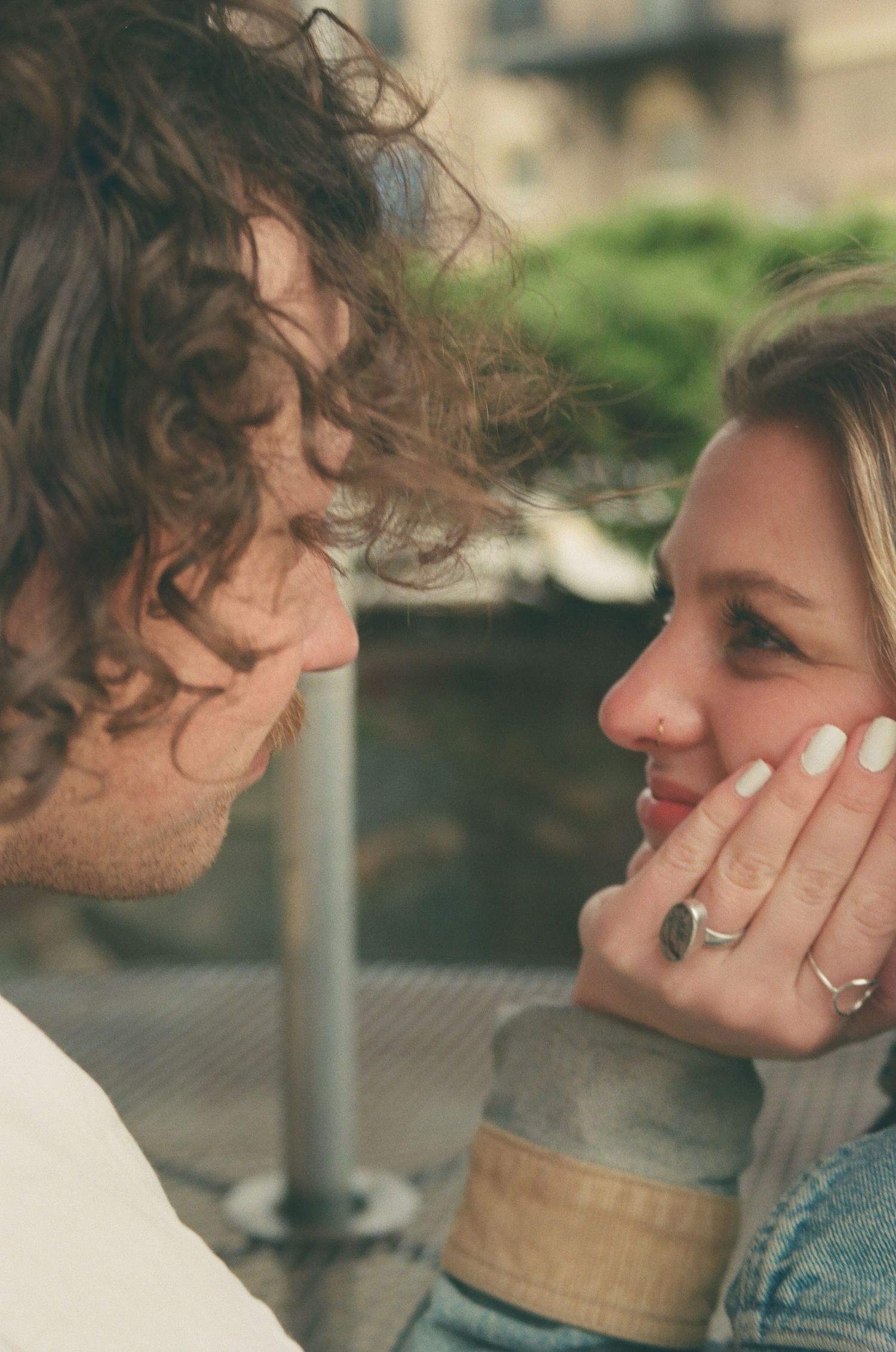 Close-up of smiling couple gazing at each other, woman showing off her engagement ring on her hand.