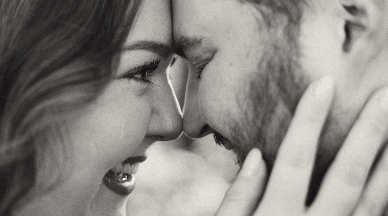 A romantic black and white close-up of a couple nearly kissing, faces touching intimately.