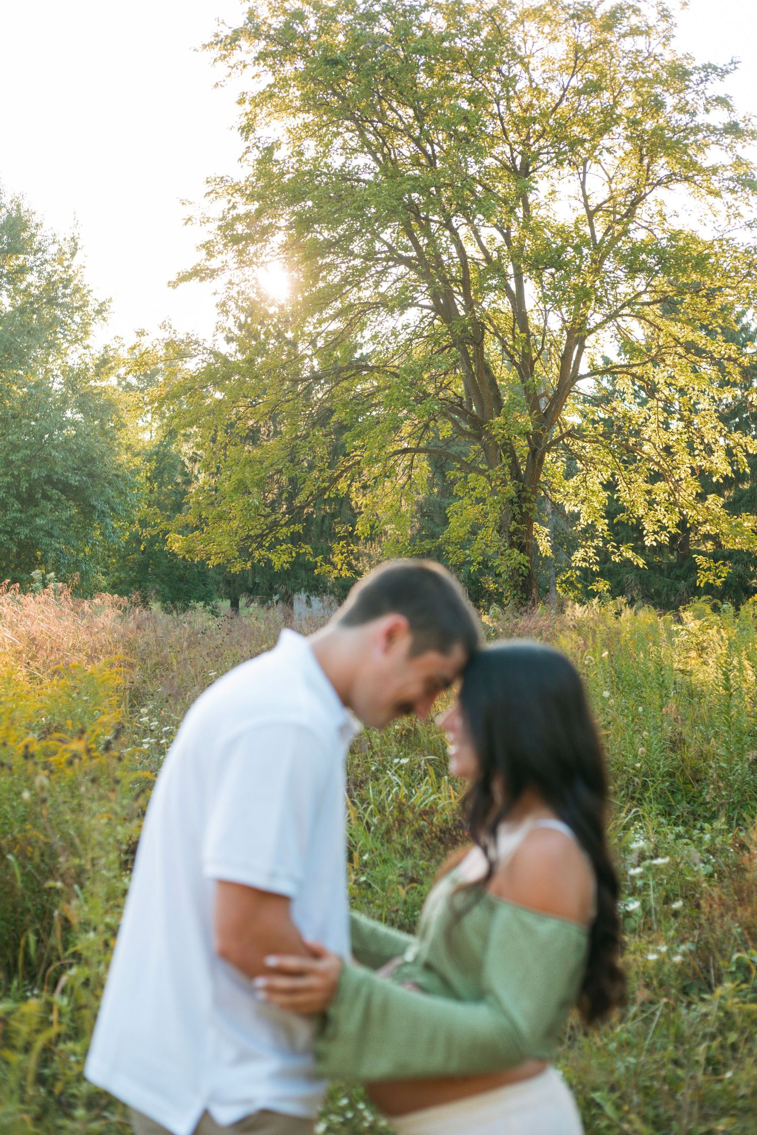 Soft focus maternity photo of couple touching foreheads in a sun-drenched wildflower meadow.