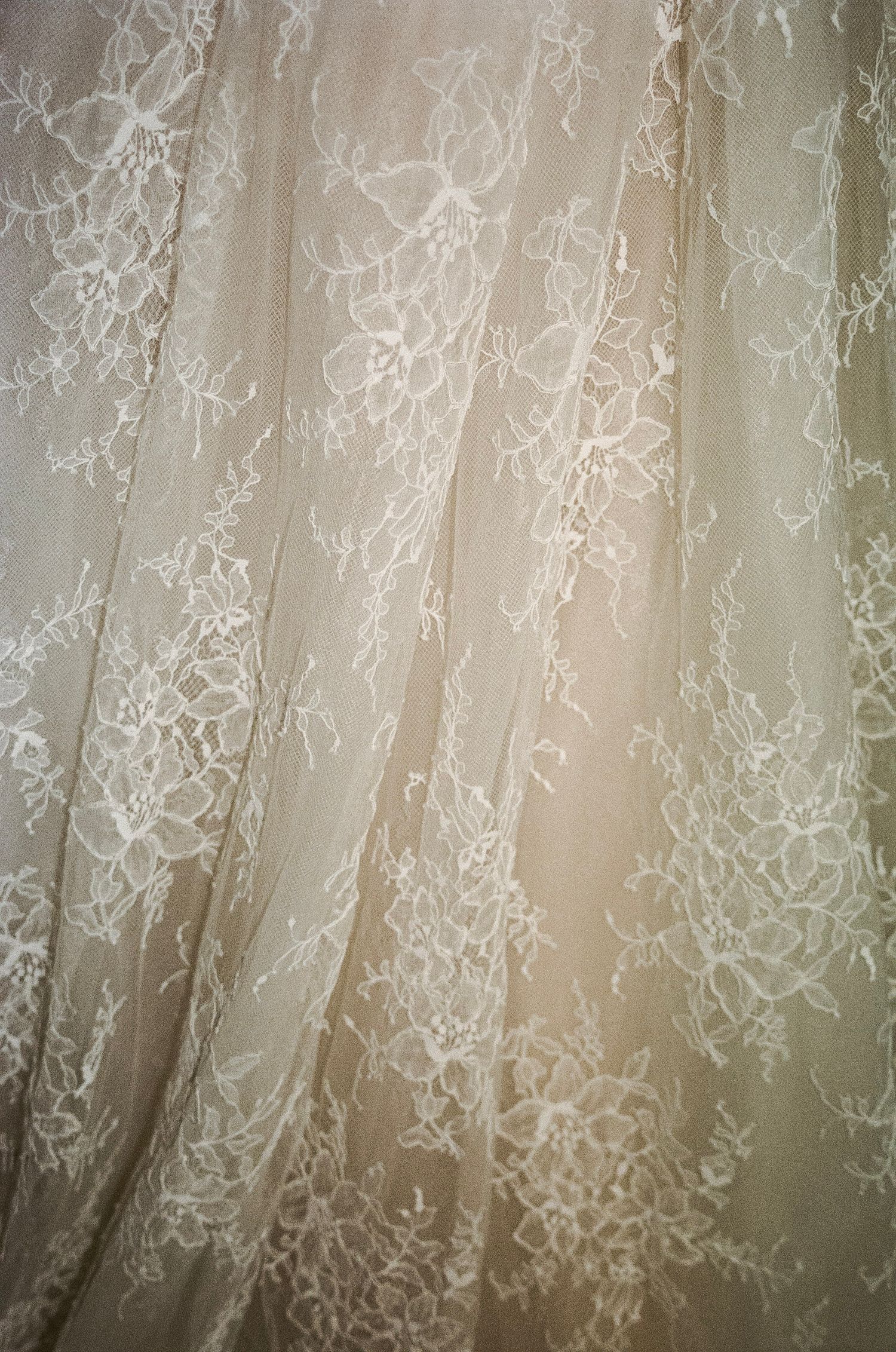 Delicate ivory lace fabric with intricate floral embroidery pattern, draped elegantly for a bridal wedding gown.