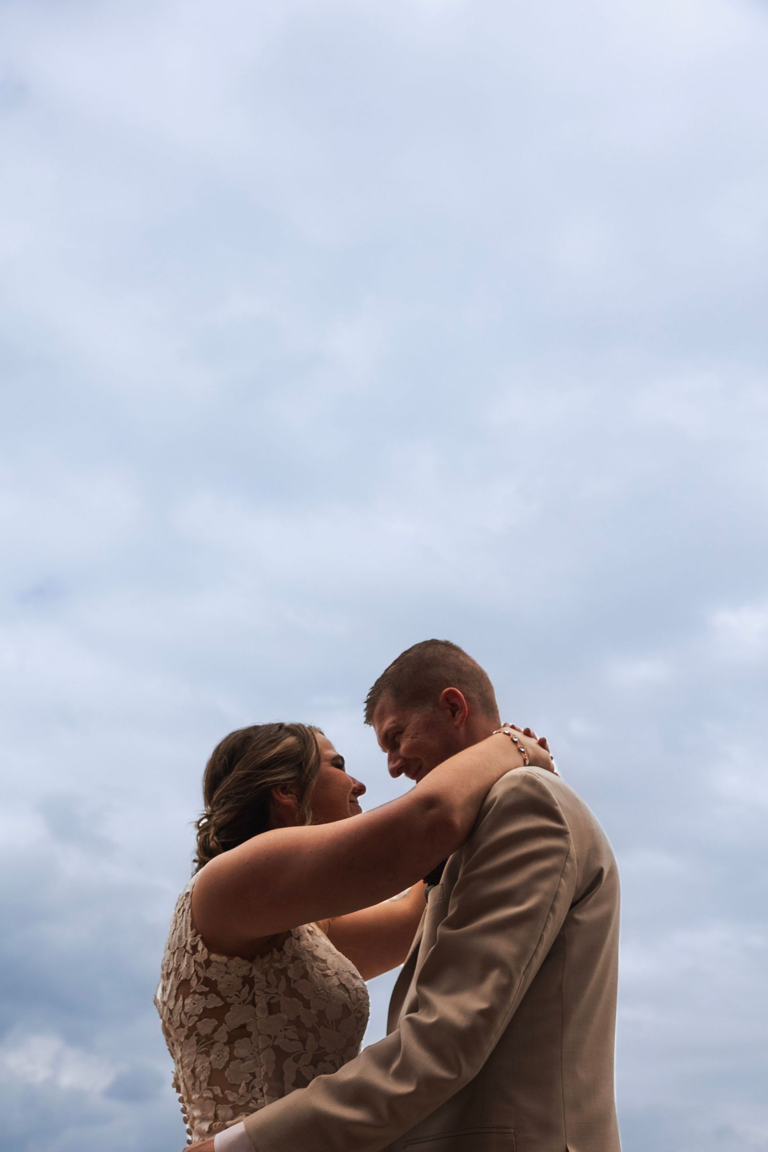Bride and groom share an intimate moment dancing together against a dramatic cloudy sky backdrop.