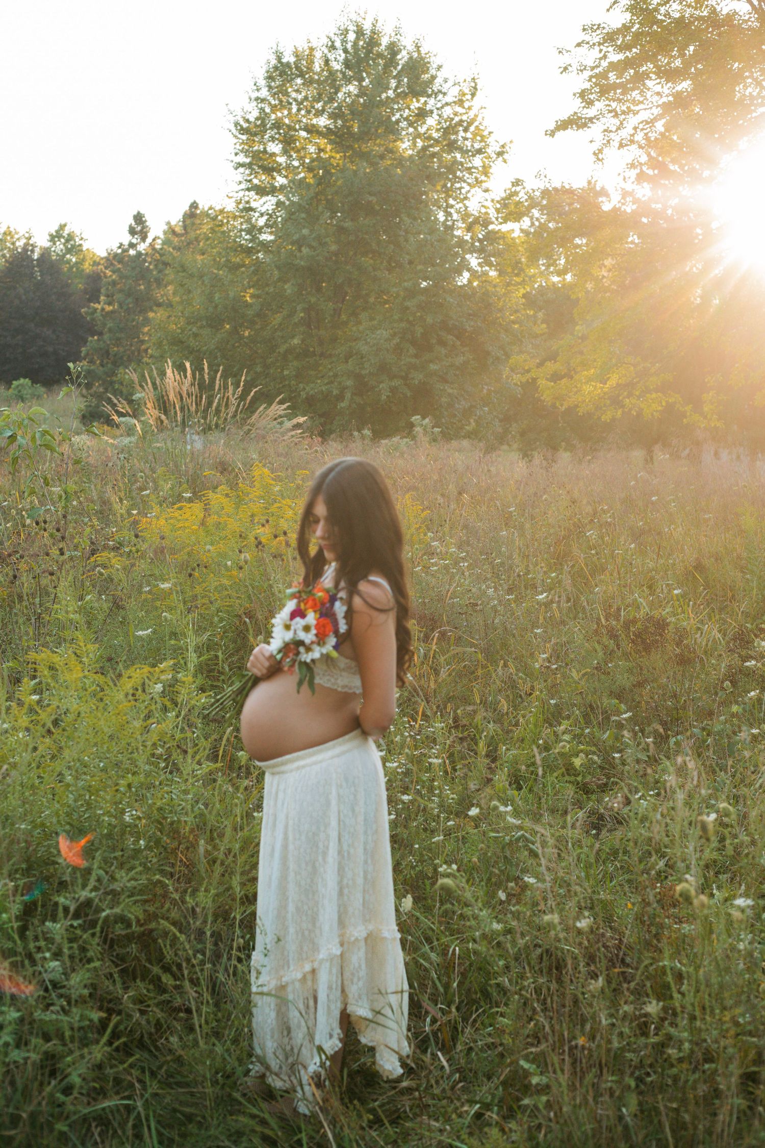 Pregnant woman holding colorful wildflower bouquet in golden sunlit meadow during maternity session.