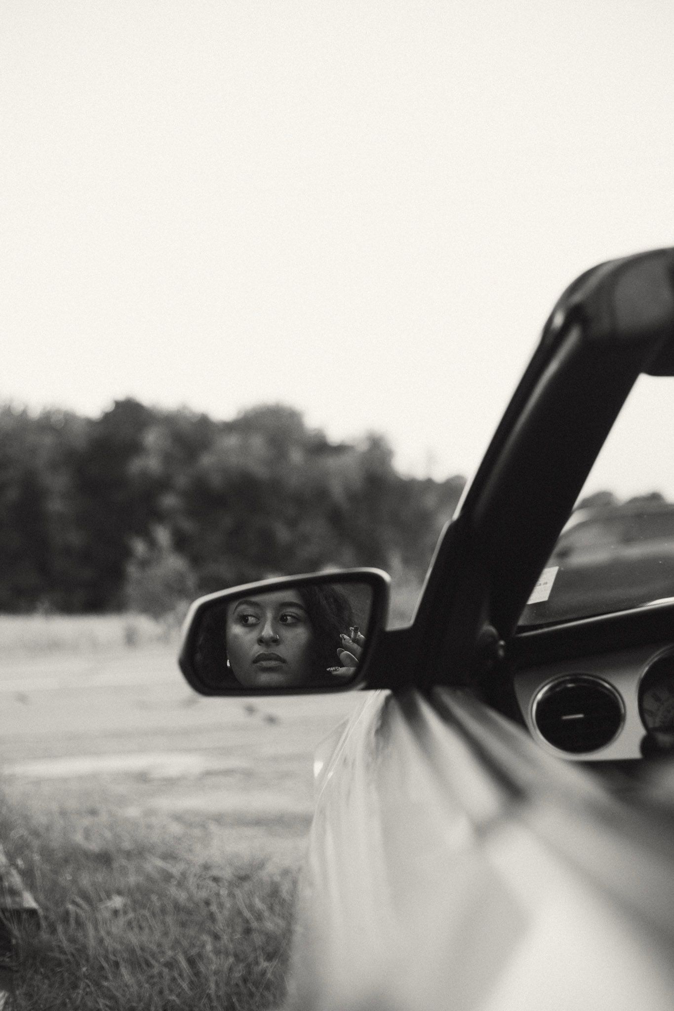 Black and white portrait of a woman reflected in a car side mirror outdoors.