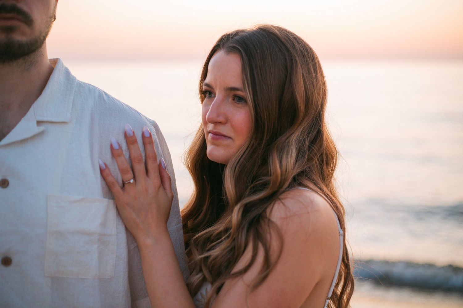 Woman with long brown hair holding mans arm at sunset on a beach.