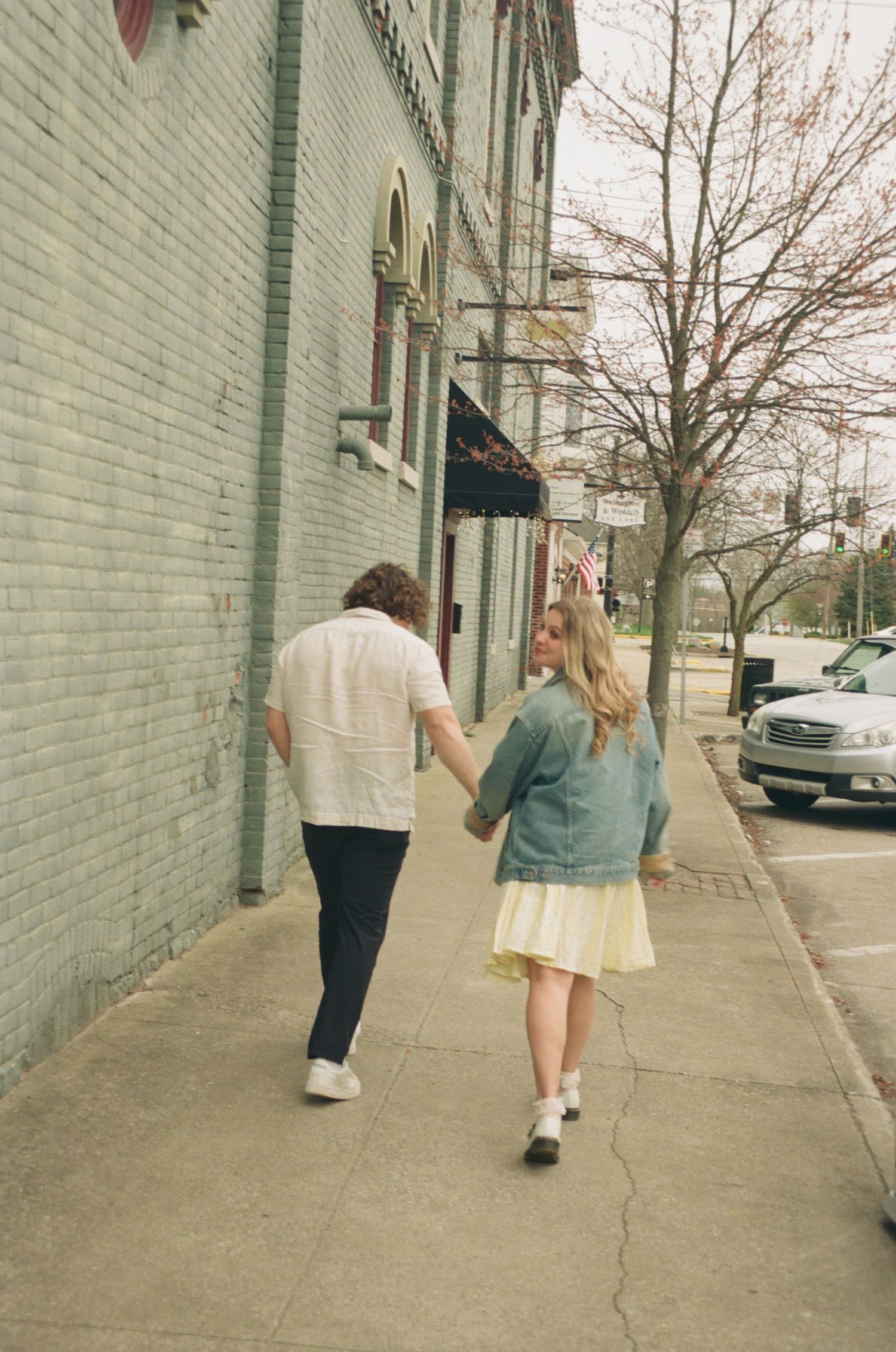Couple holding hands while strolling along a charming brick building sidewalk in early spring.