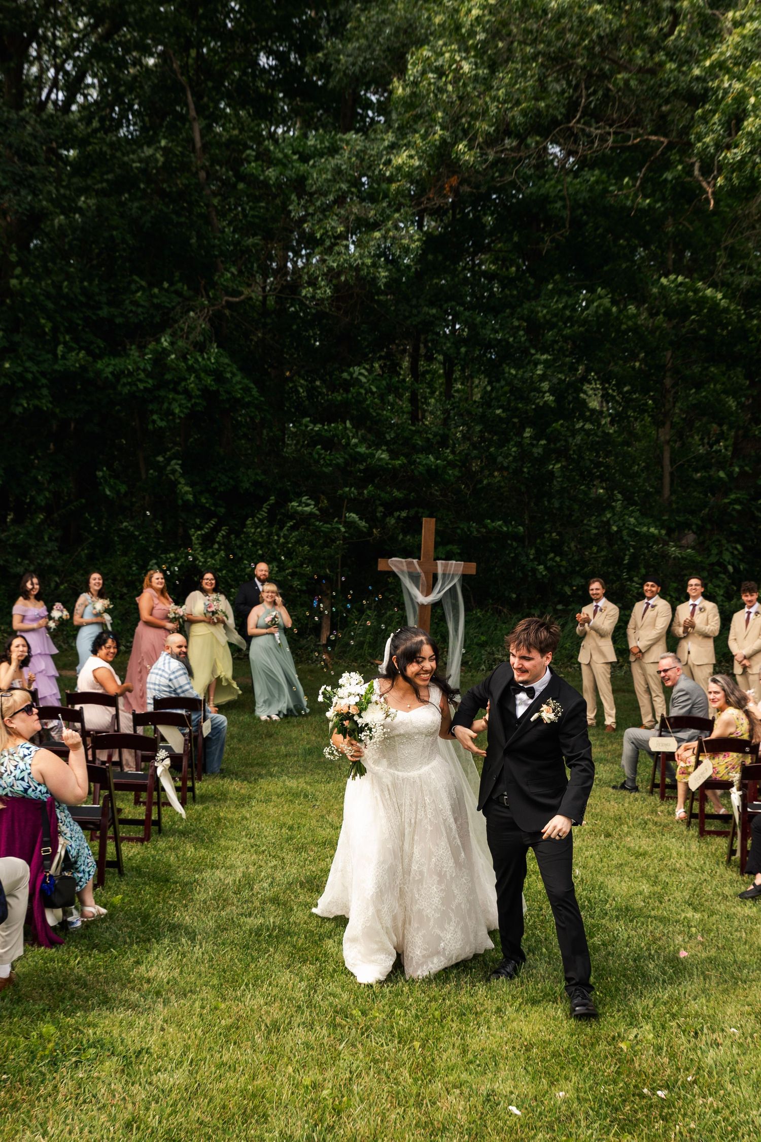 A joyful bride and groom walk back down the aisle after an outdoor garden wedding ceremony with guests.