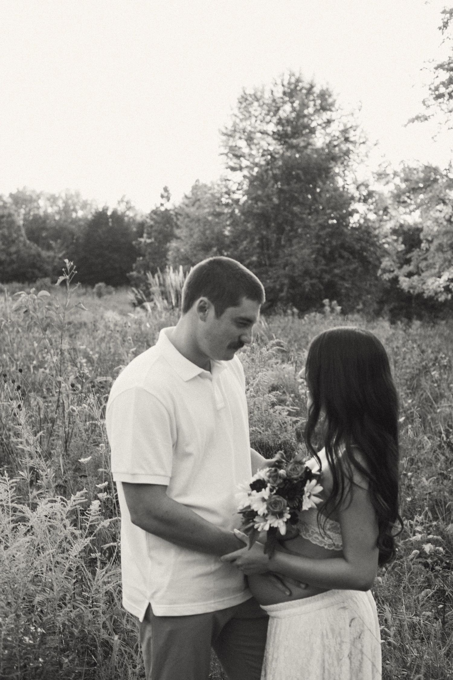 Black and white photo of couple holding wildflower bouquet together in a lush meadow.