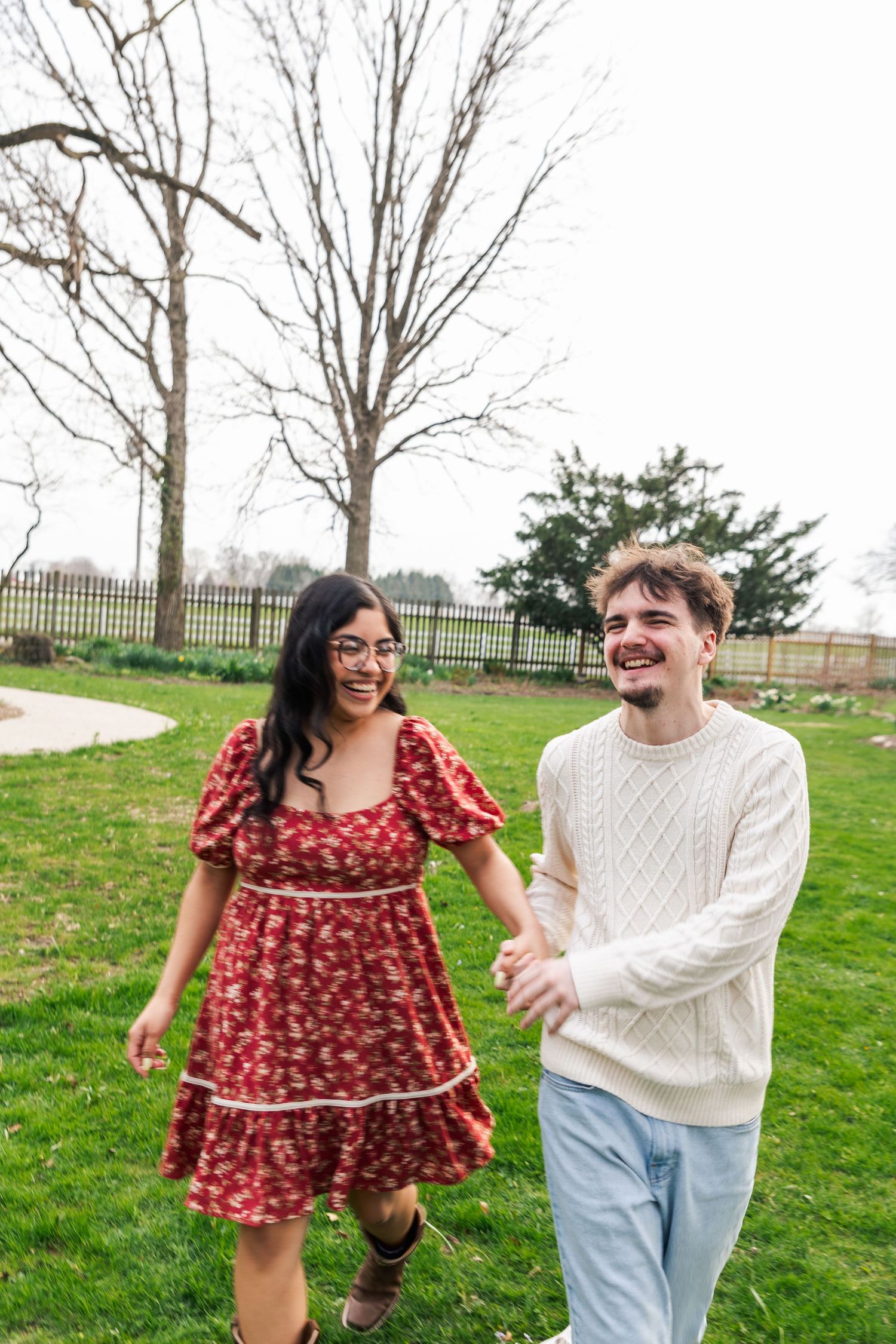 Laughing couple holding hands and walking through a green park on a cloudy day.