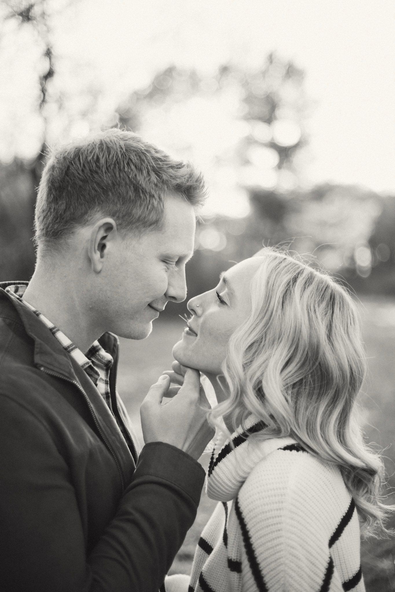Black and white romantic photo of couple nearly kissing in a sun-drenched outdoor setting.