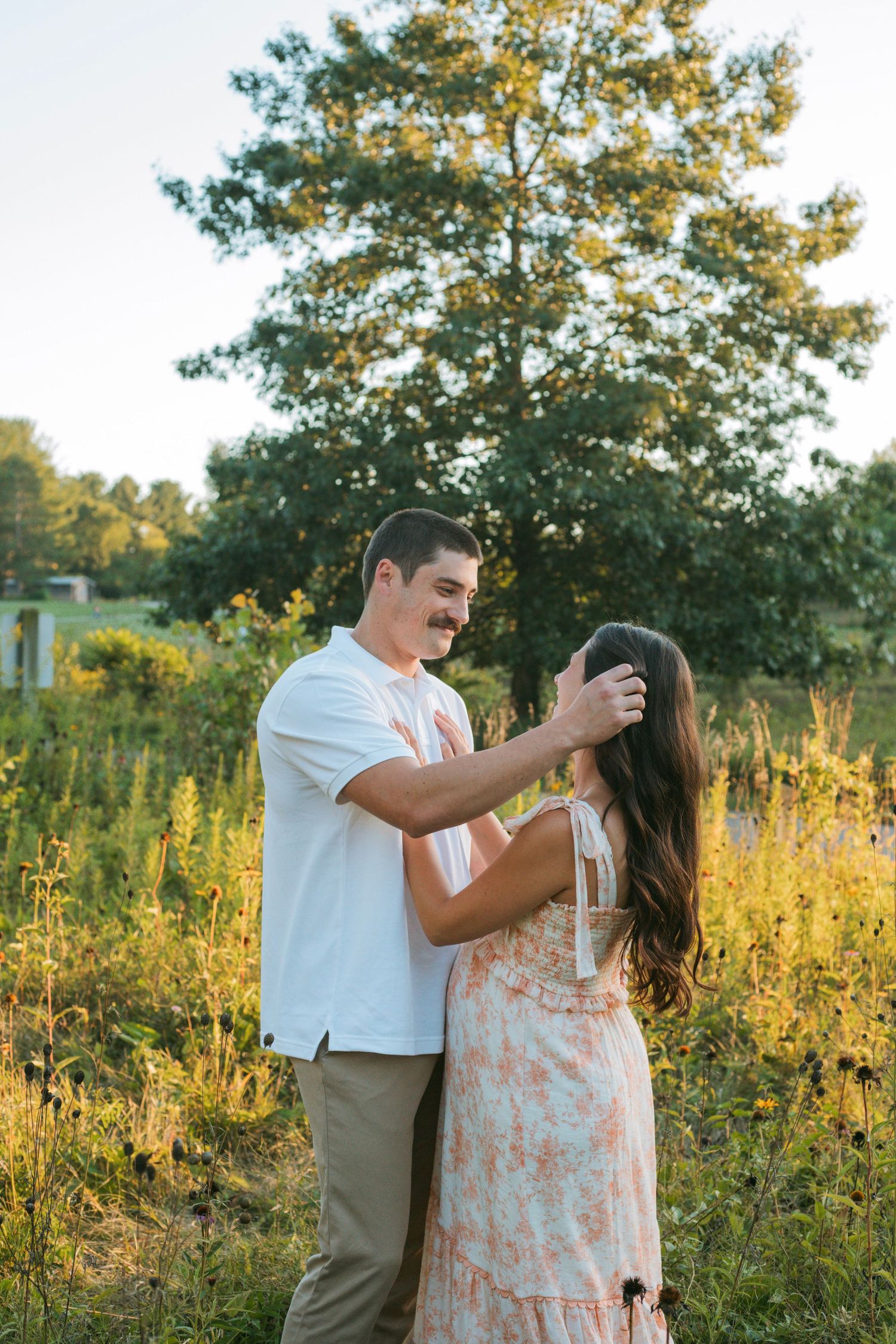 Man gently touching pregnant partners hair in sun-drenched wildflower field during outdoor maternity shoot.