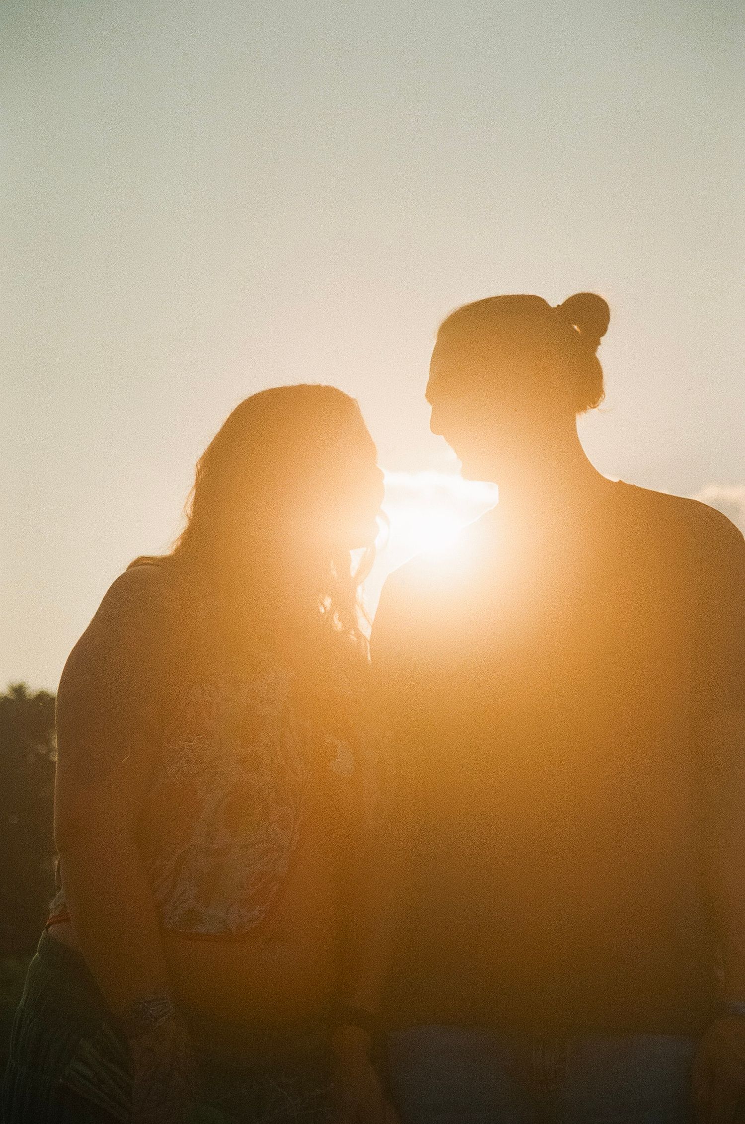 Silhouette of a couple facing each other backlit by a golden sunset, creating a romantic warm glow.
