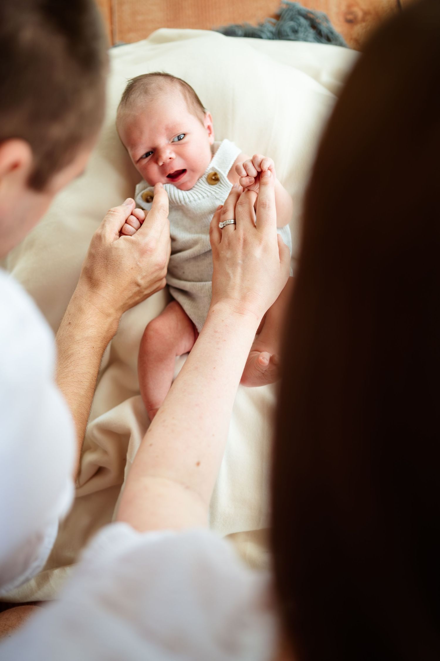 Close-up shots of playful interaction between parent and baby on white bedding.