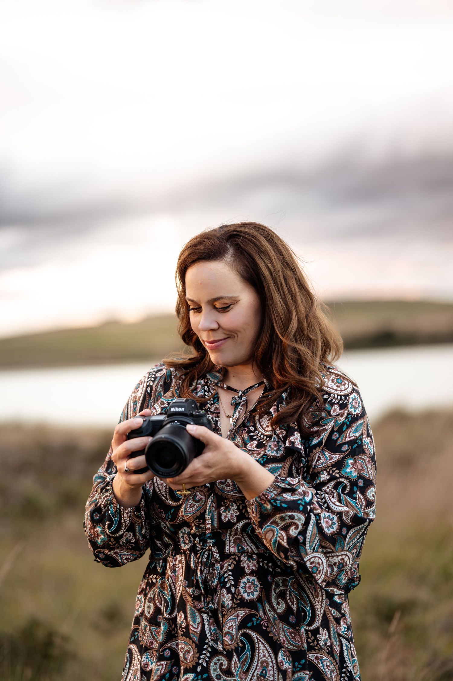 A photographer in a patterned dress works with a camera in an outdoor setting.