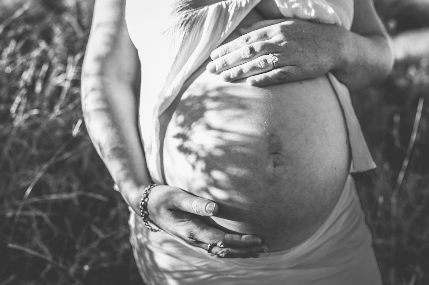 Black and white close-up of hands cradling pregnant belly during maternity session.