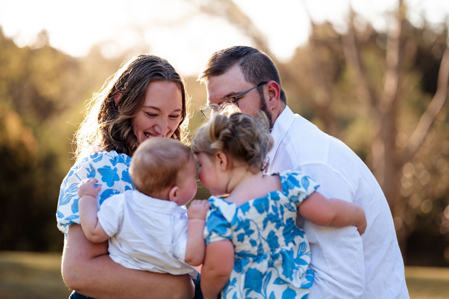 Family sharing tender moments during outdoor portrait session in blue and white outfits.