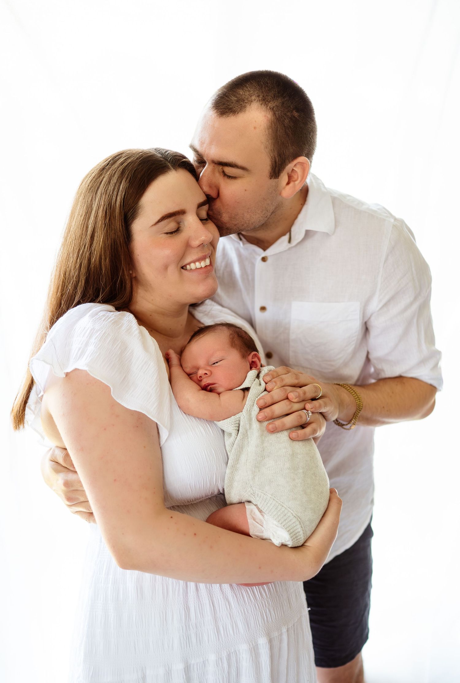 Loving family portrait series with newborn baby in white studio setting.