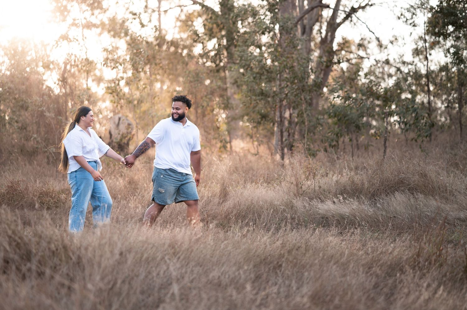 Couple walking through tall grass in a natural outdoor setting during golden hour.
