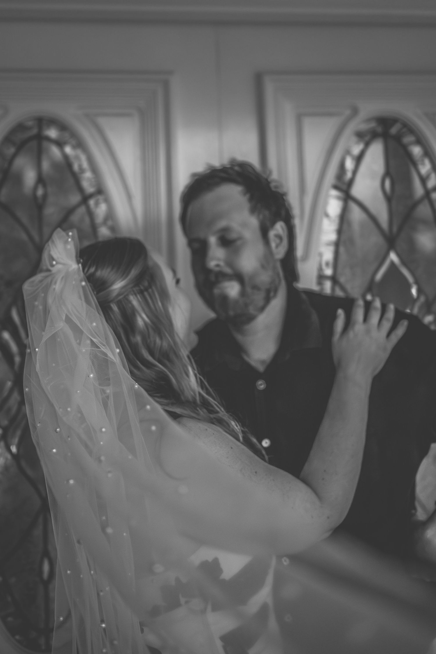 An intimate black and white portrait of a couple in front of stained glass windows.