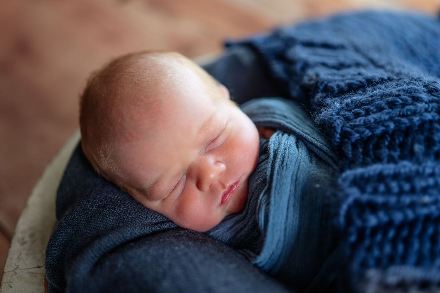 Close-up portrait of sleeping newborn wrapped in navy blue textured blanket.