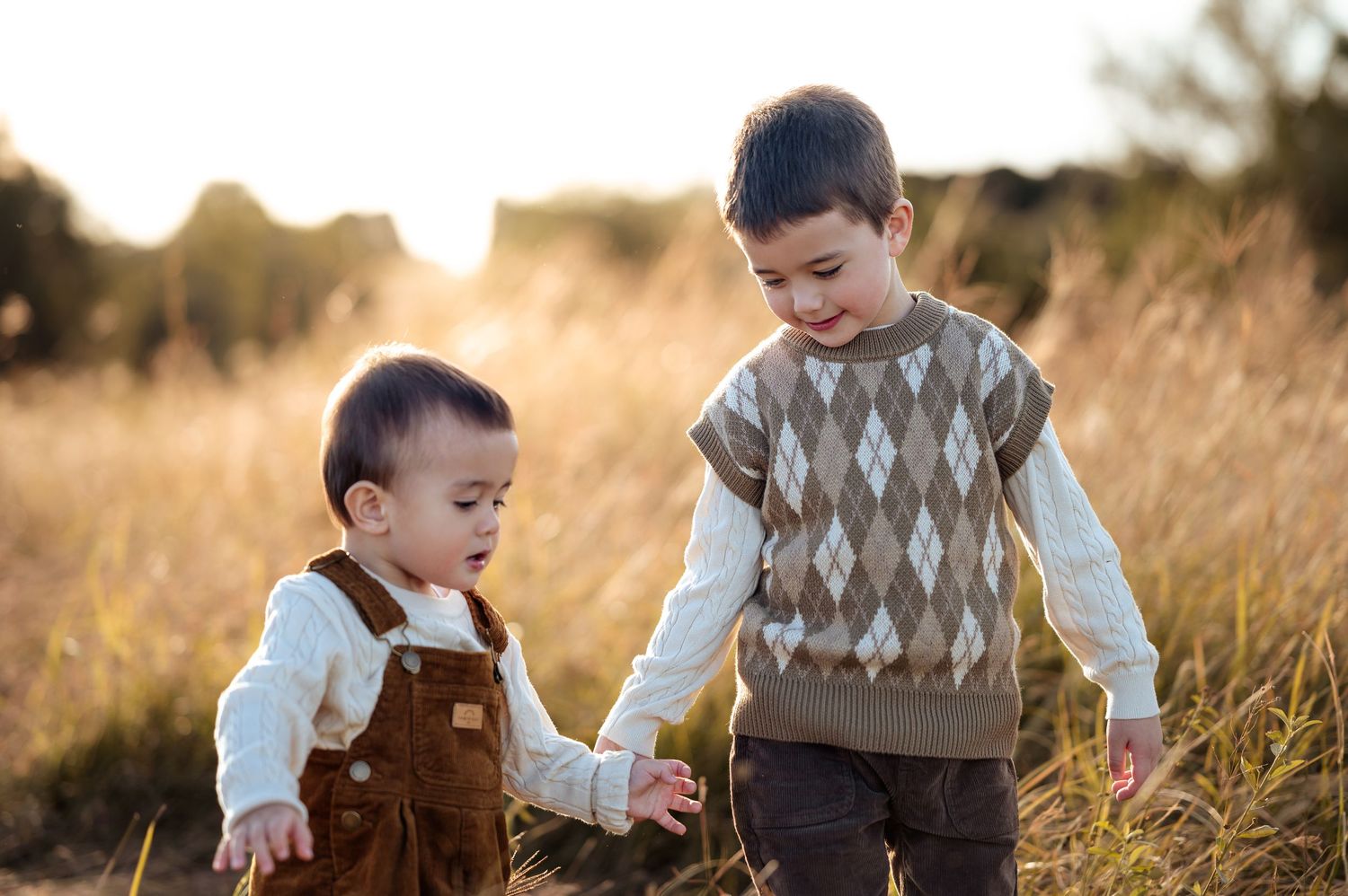 Two children in argyle sweaters exploring outdoors during golden hour.