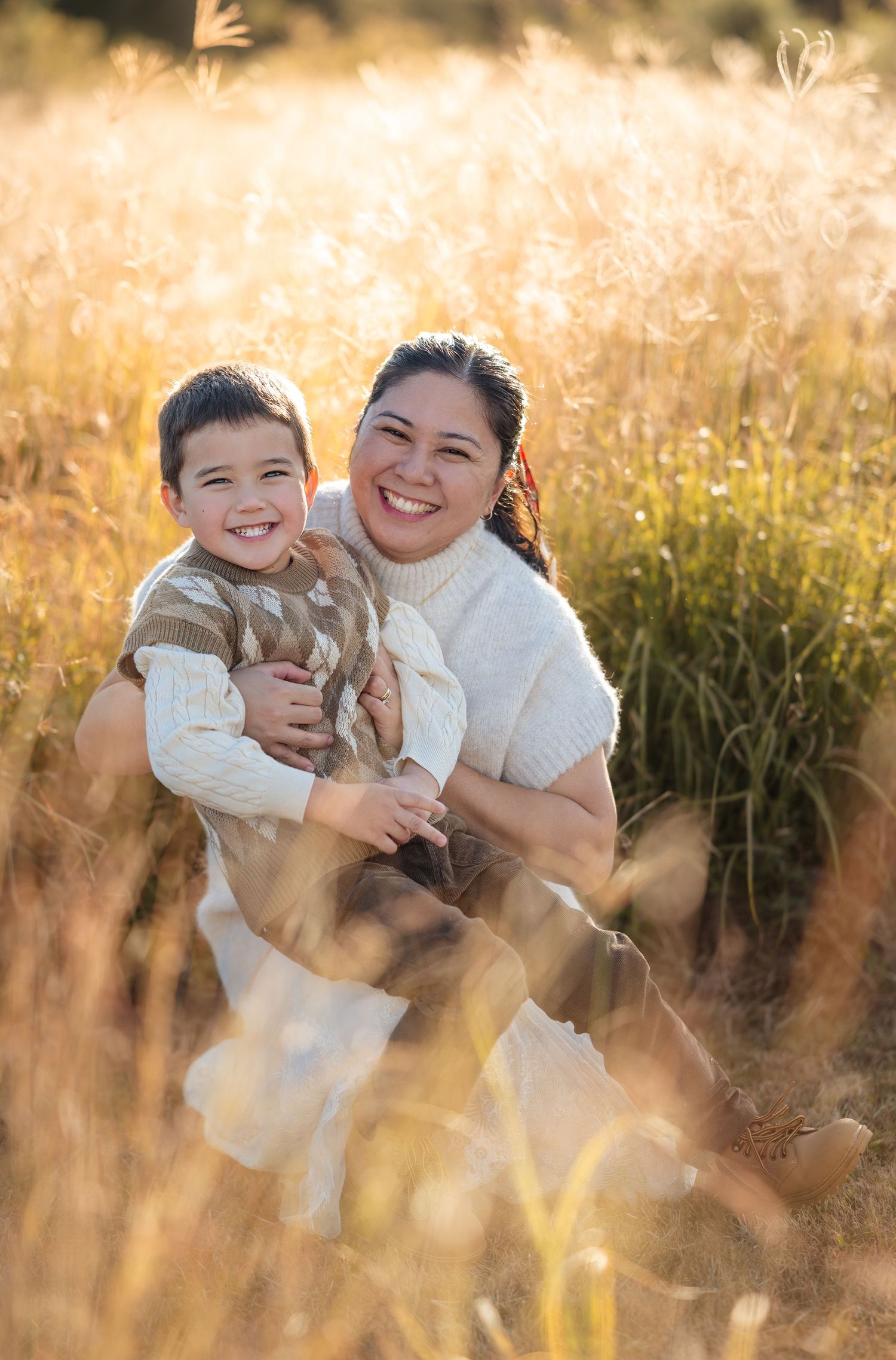 A joyful outdoor family photoshoot in a golden field at sunset with warm lighting and natural expressions.