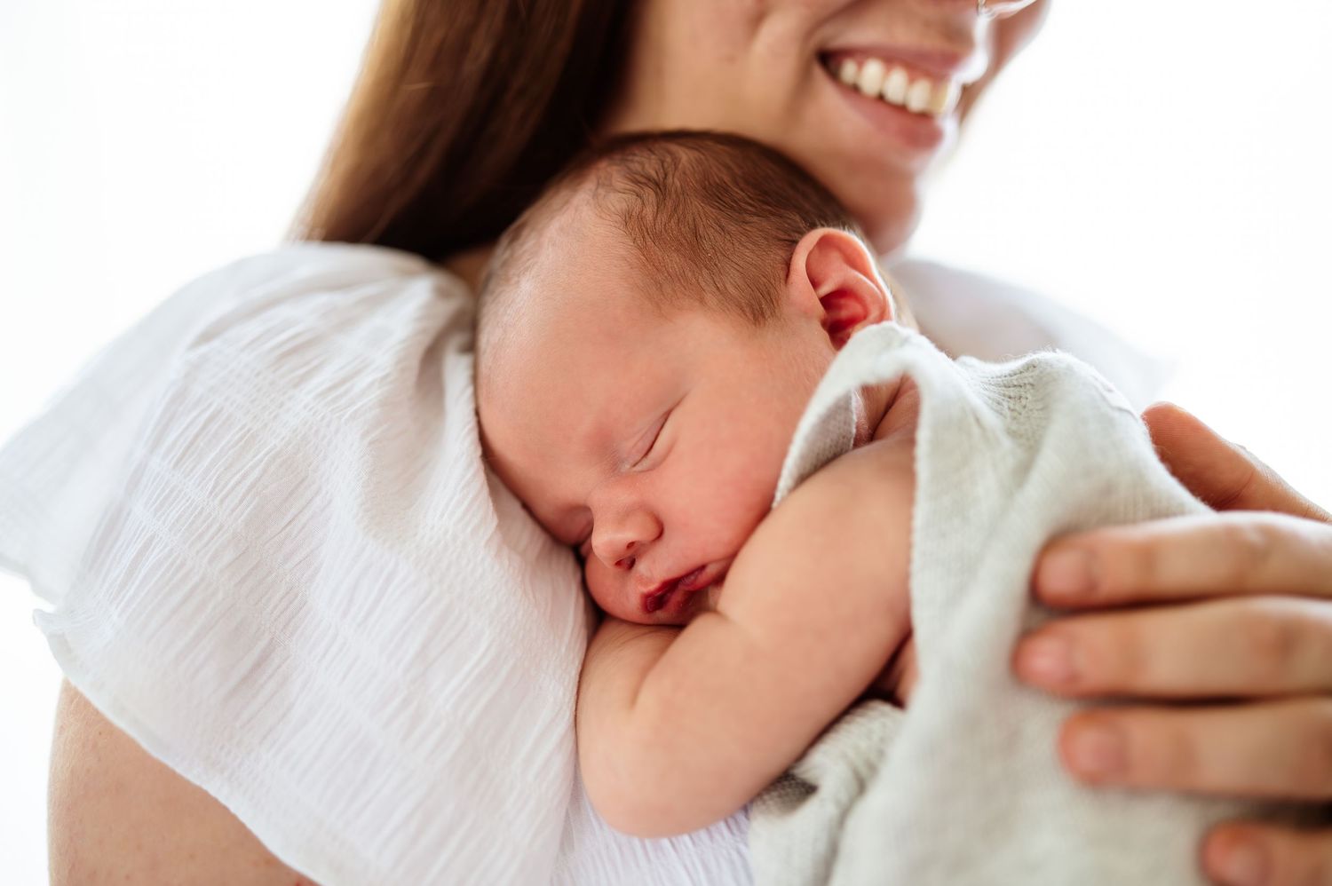 Newborn baby resting peacefully on white blanket with soft natural lighting.