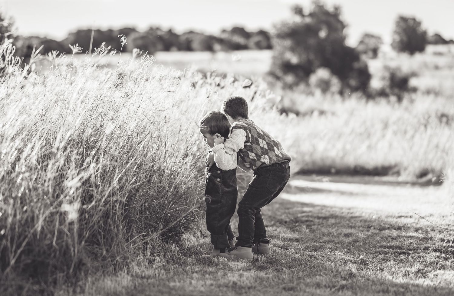 Black and white silhouettes of people embracing in a field at sunset.