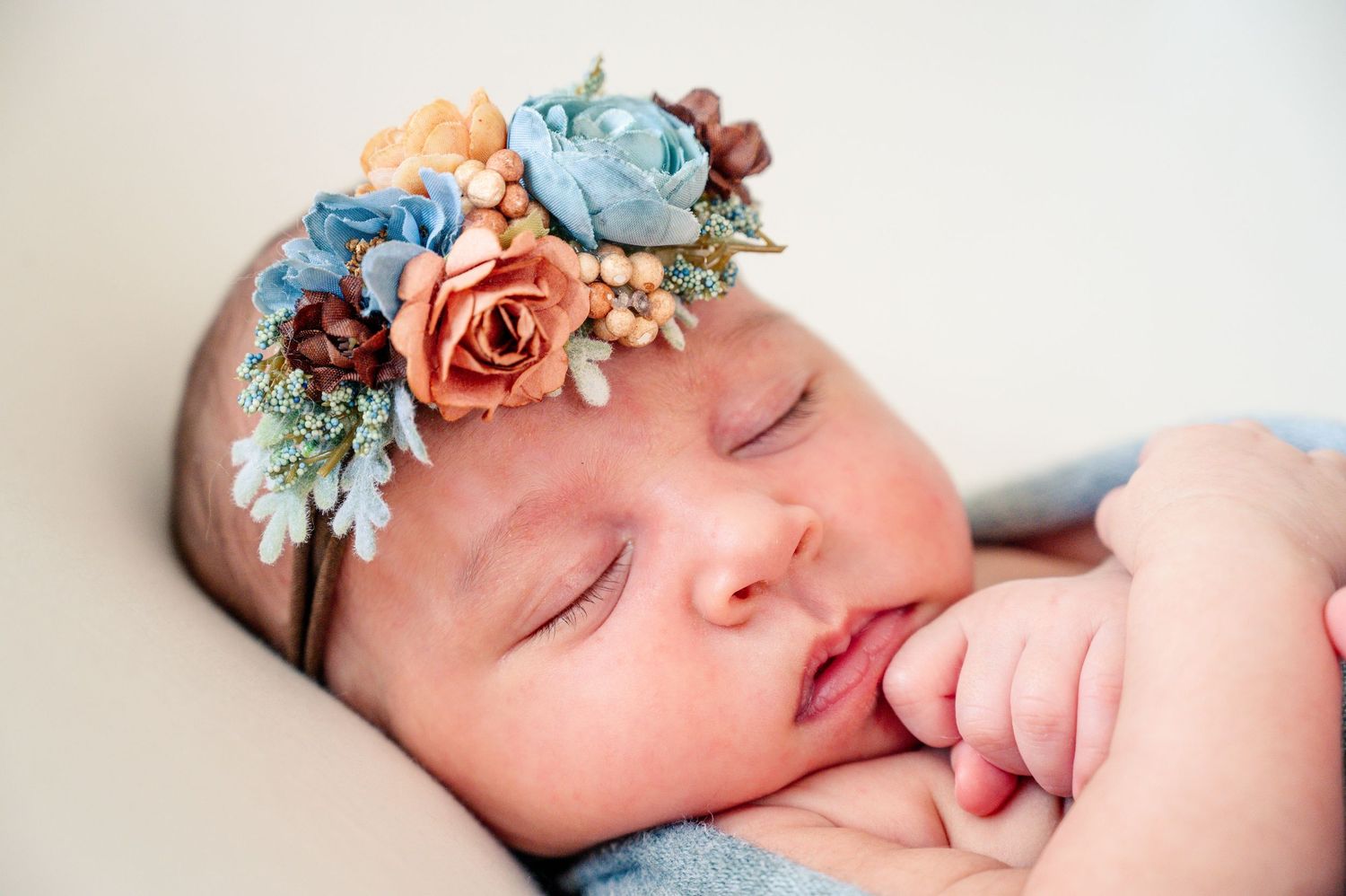 Peaceful sleeping newborn wearing delicate floral headband in soft lighting.
