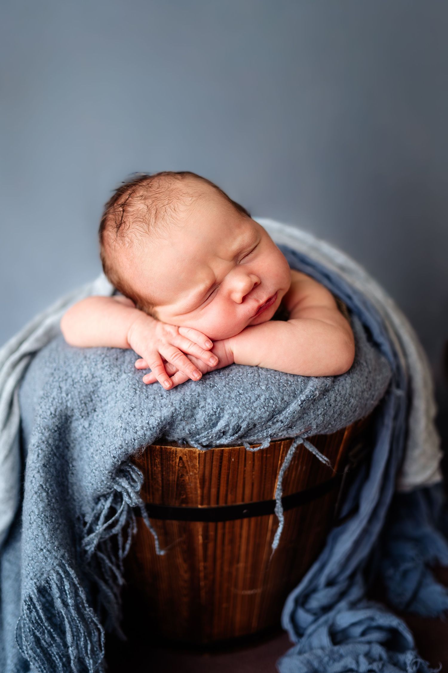 Sleeping newborn wrapped in gray blanket on wooden surface.